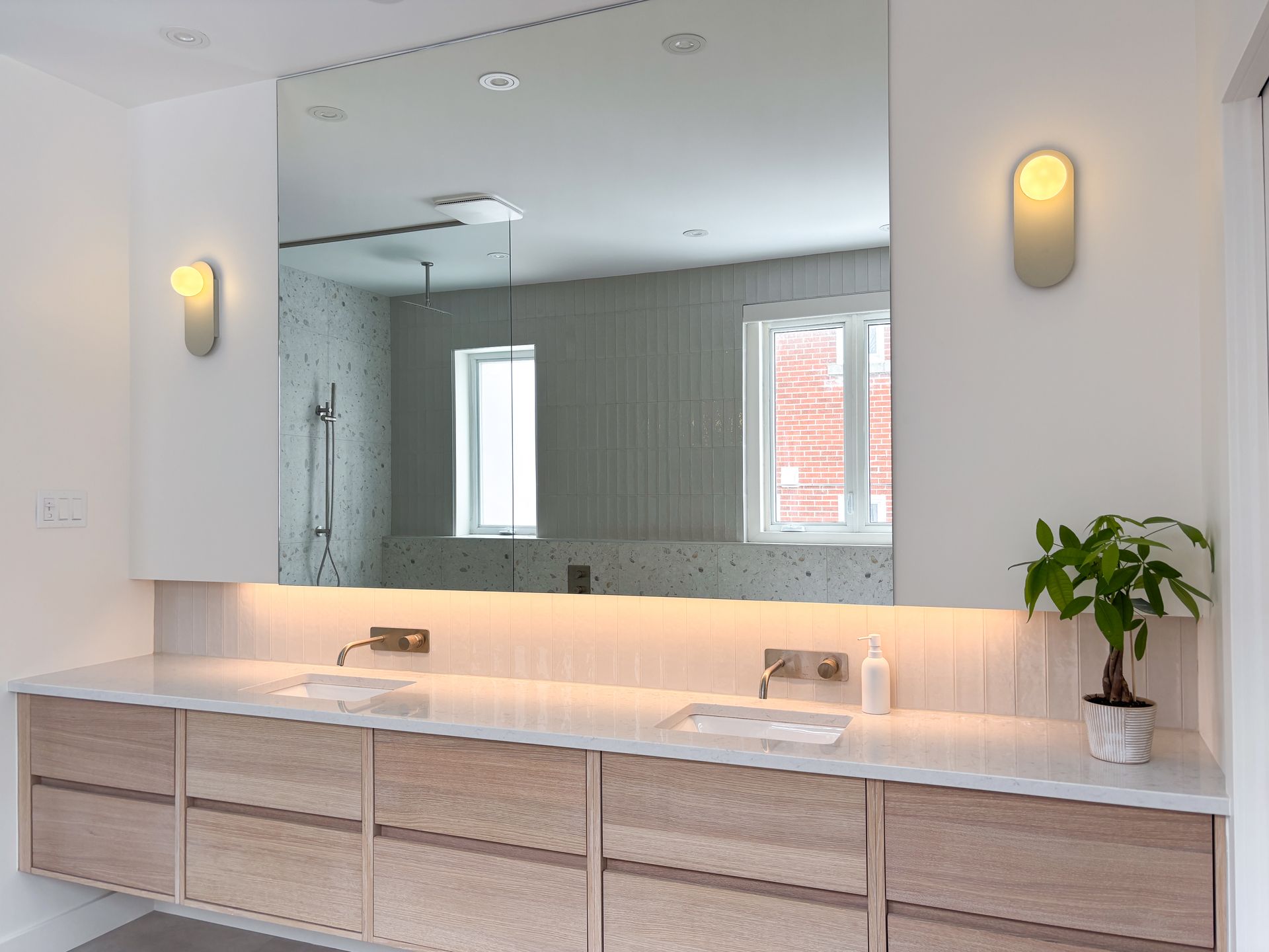 Salle de bain moderne avec grand miroir, double vasque, armoires en bois clair et deux appliques.