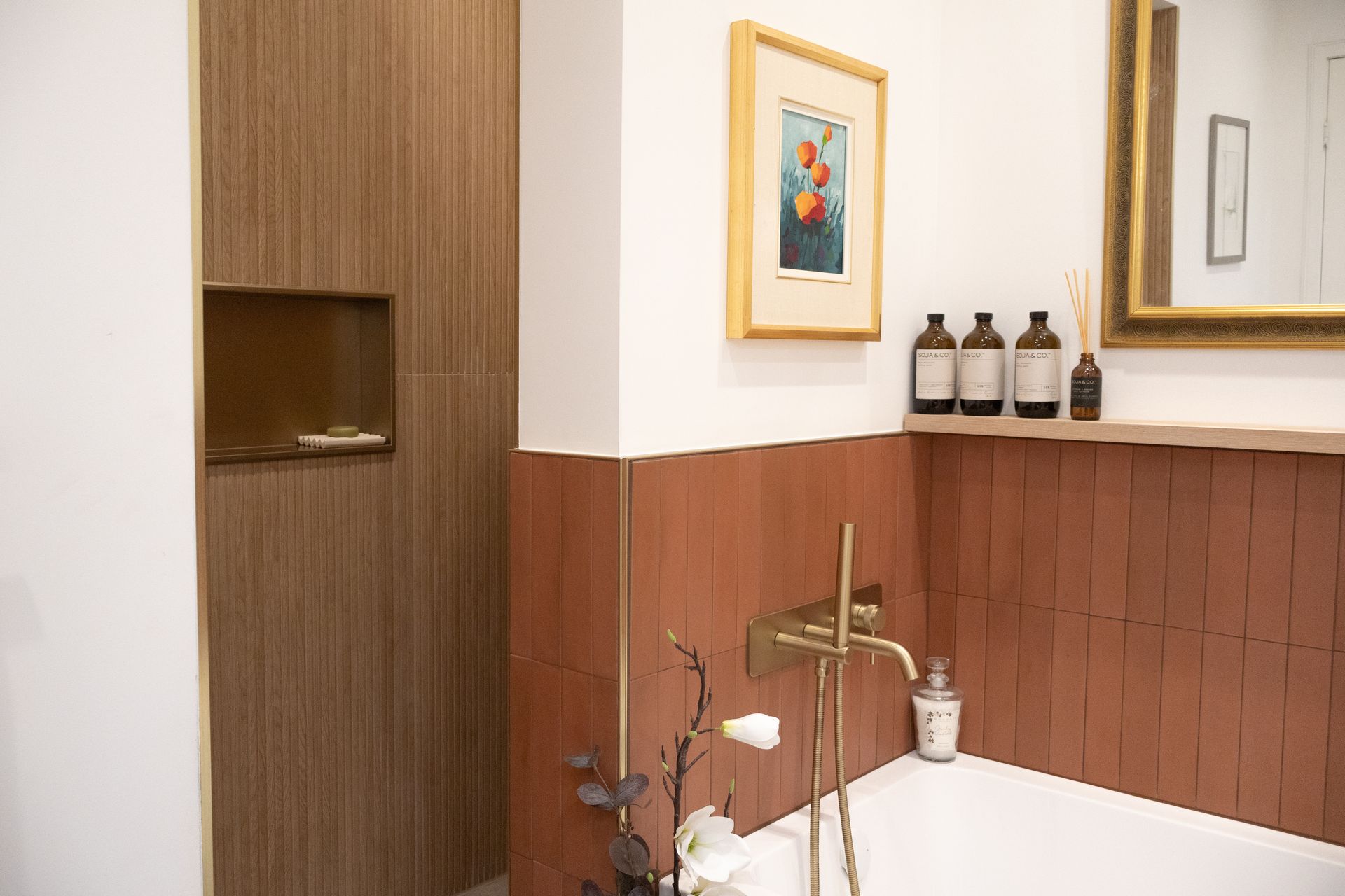 Salle de bain avec carrelage en terre cuite, luminaires dorés, œuvres d'art et niche en bois.