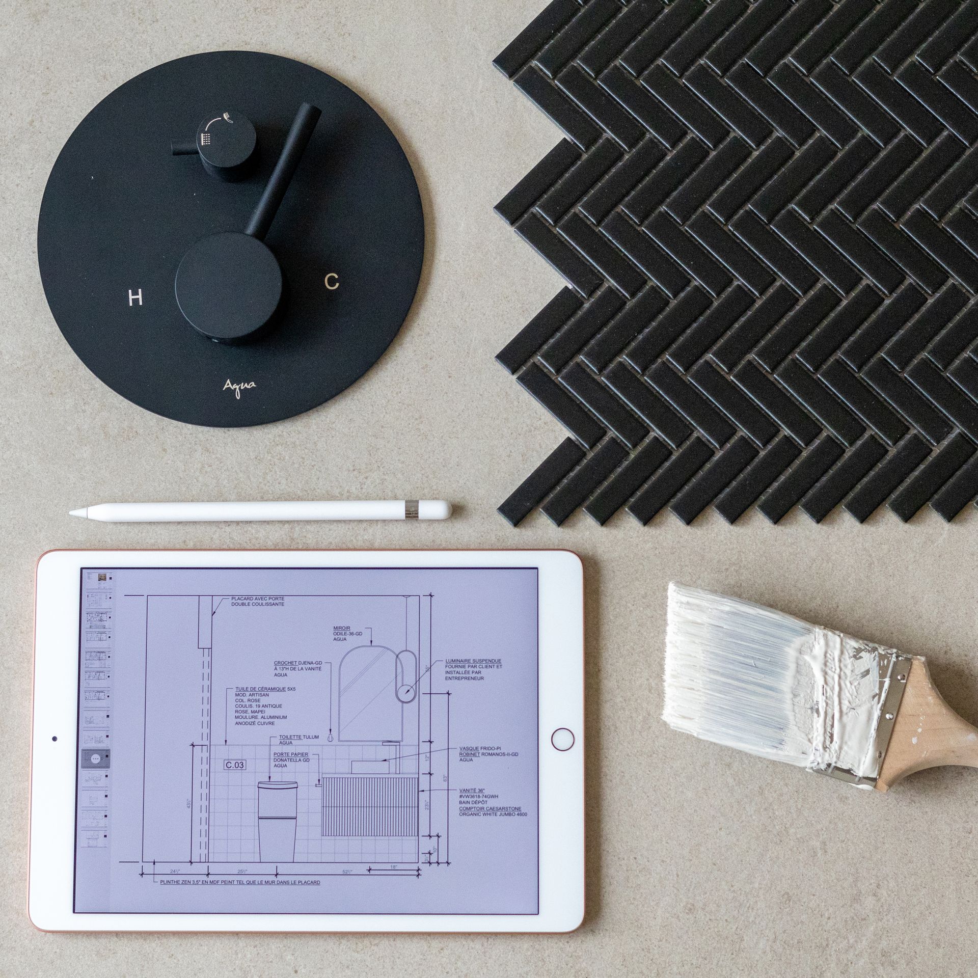 Robinet de douche noir, carrelage à chevrons, plan numérique sur tablette, pinceau et crayon sur une surface grise.
