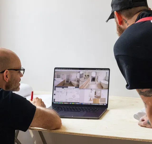 Deux personnes consultent des plans de maison sur un ordinateur portable à une table