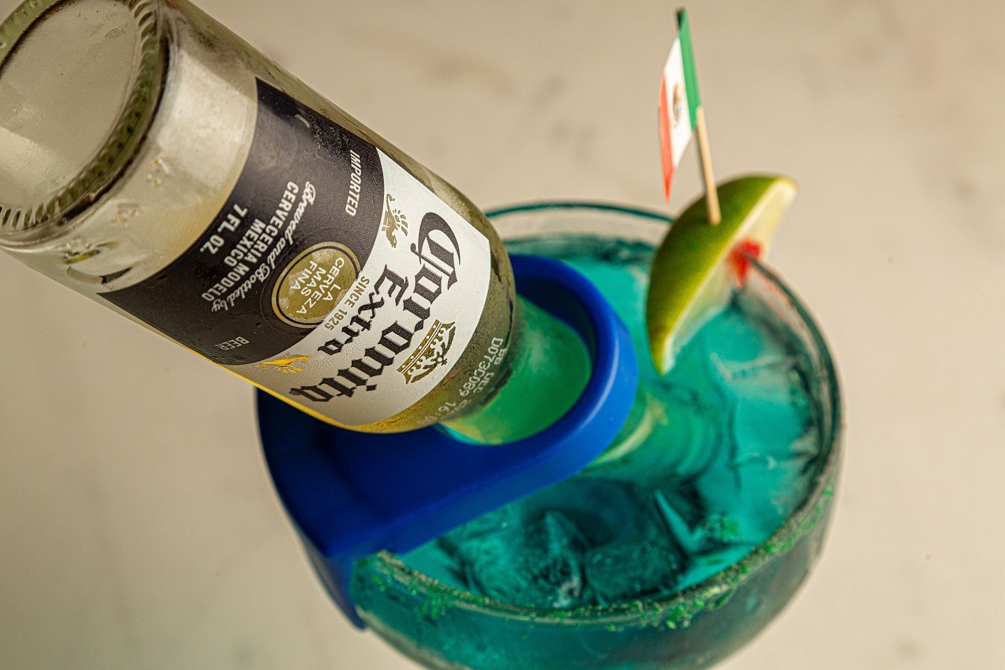 A bottle of corona extra is being poured into a blue drink.