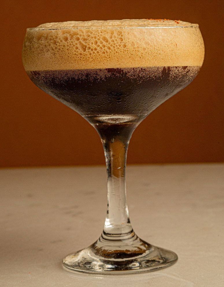 A martini glass filled with a brown liquid on a table.