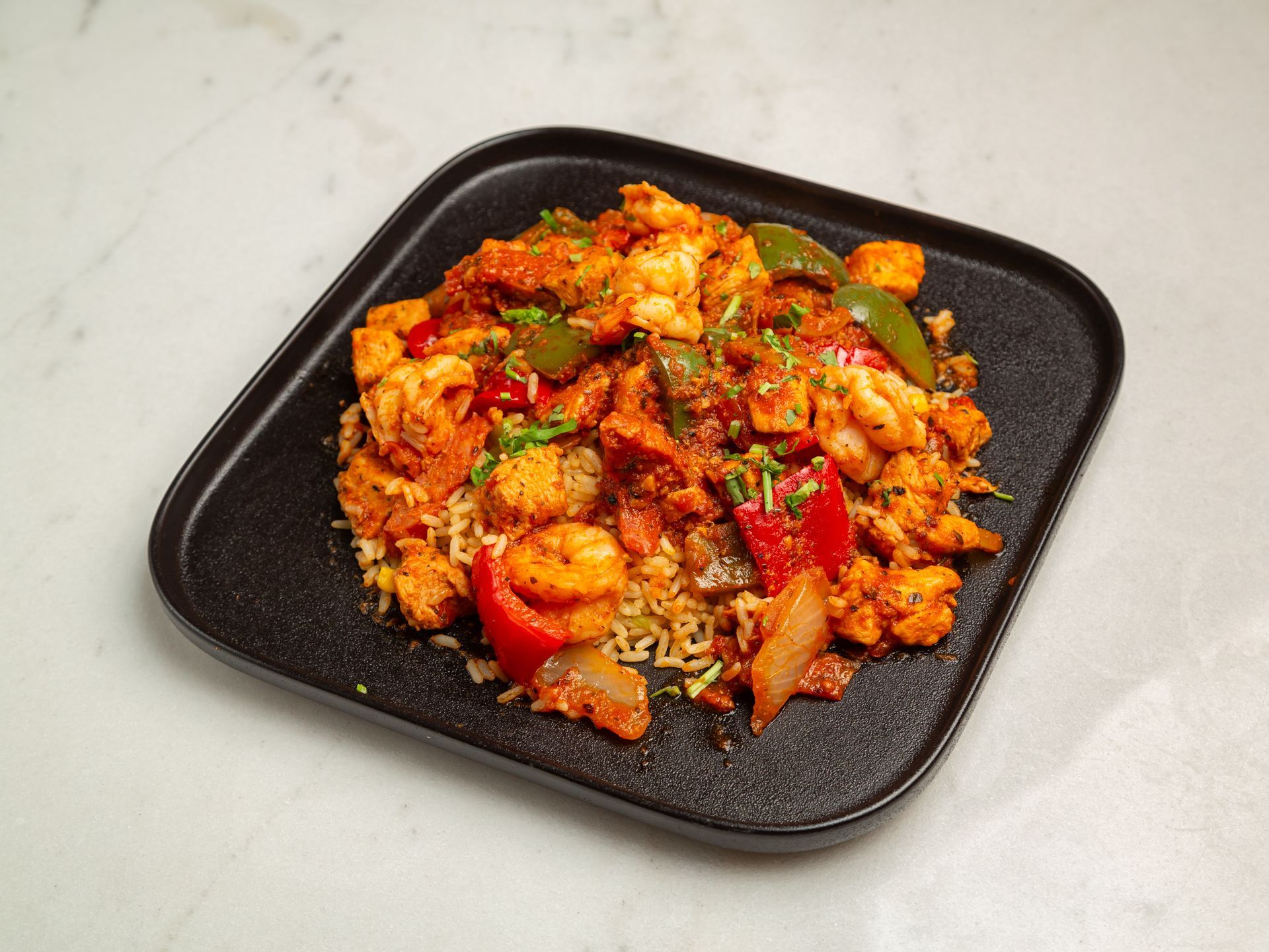 A black plate topped with chicken and vegetables on a table.