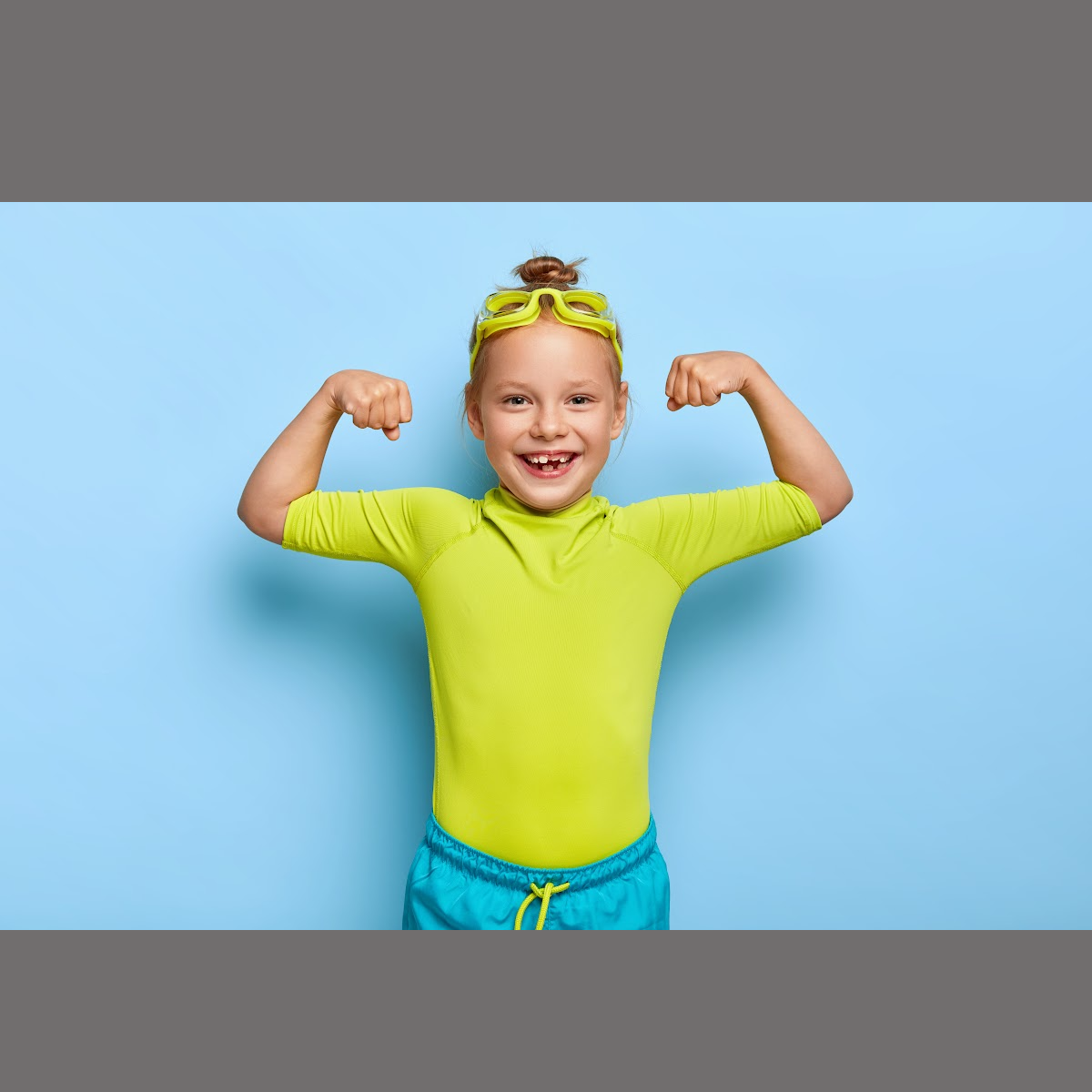 A young girl with swim goggles on making a muscle with her arms.
