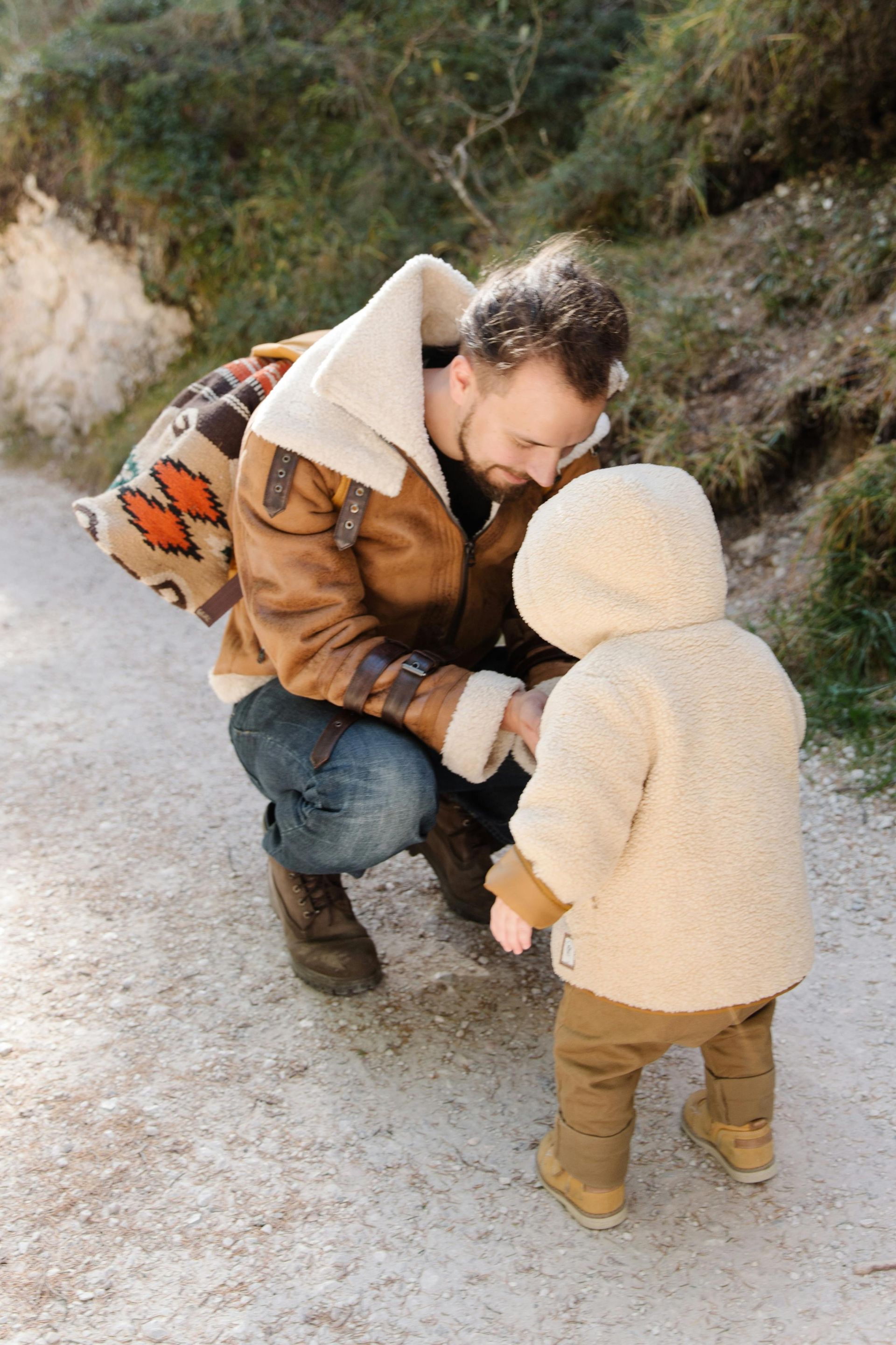 A man is kneeling down next to a small child on a dirt road.