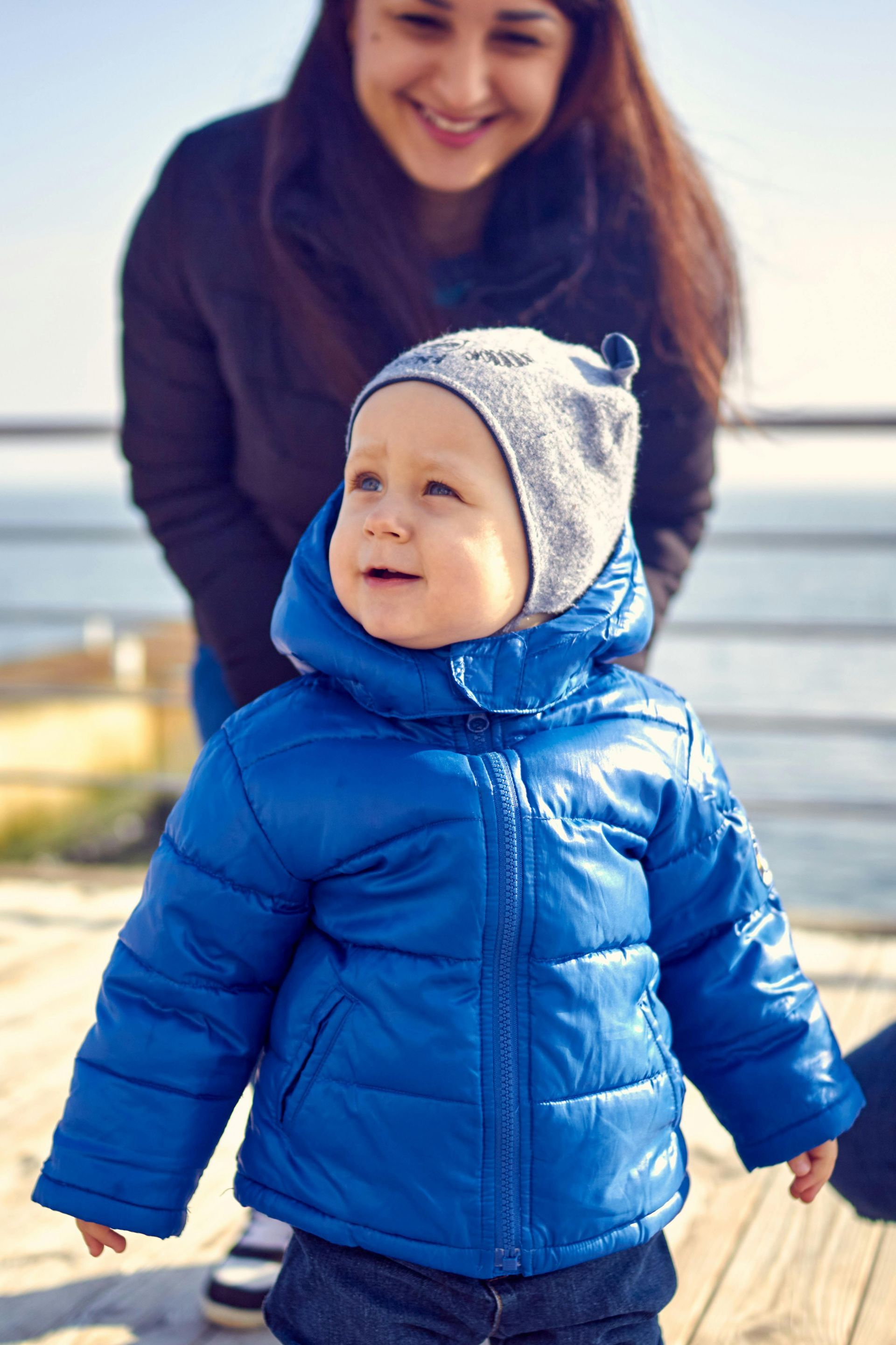 A woman is standing next to a little boy in a blue jacket.