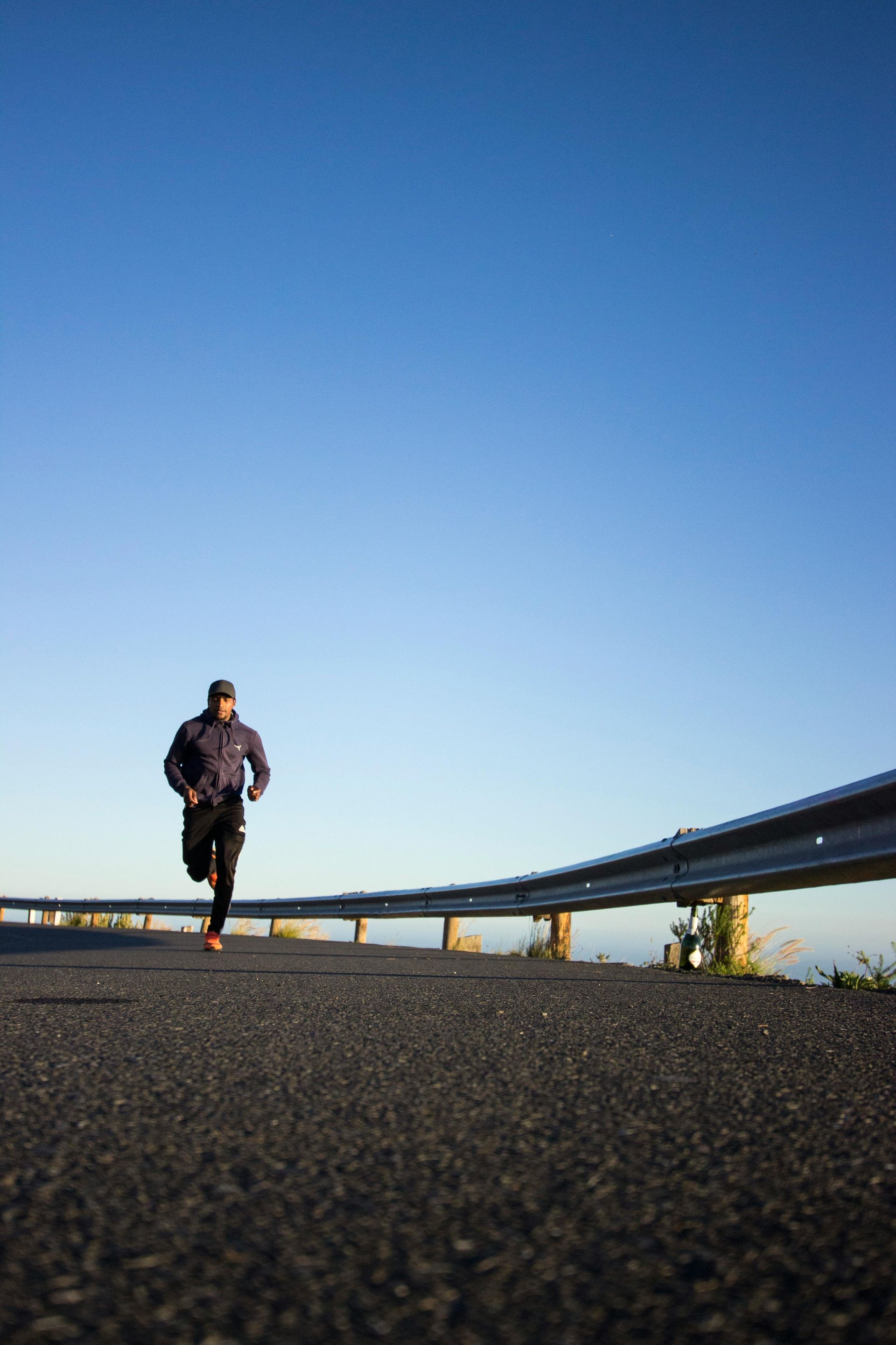 A man is running down a road next to a railing.