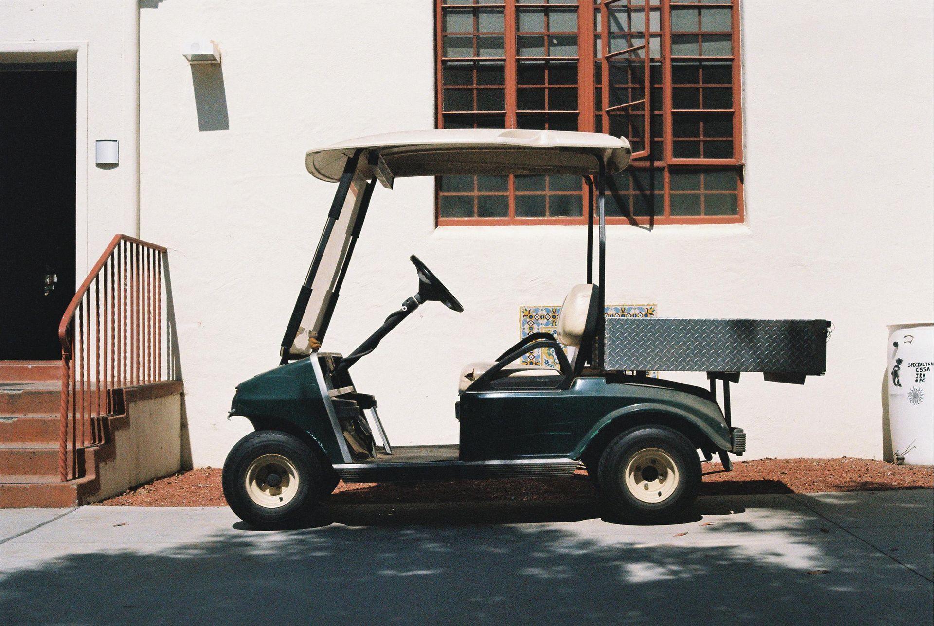 A green golf cart is parked in front of a white building