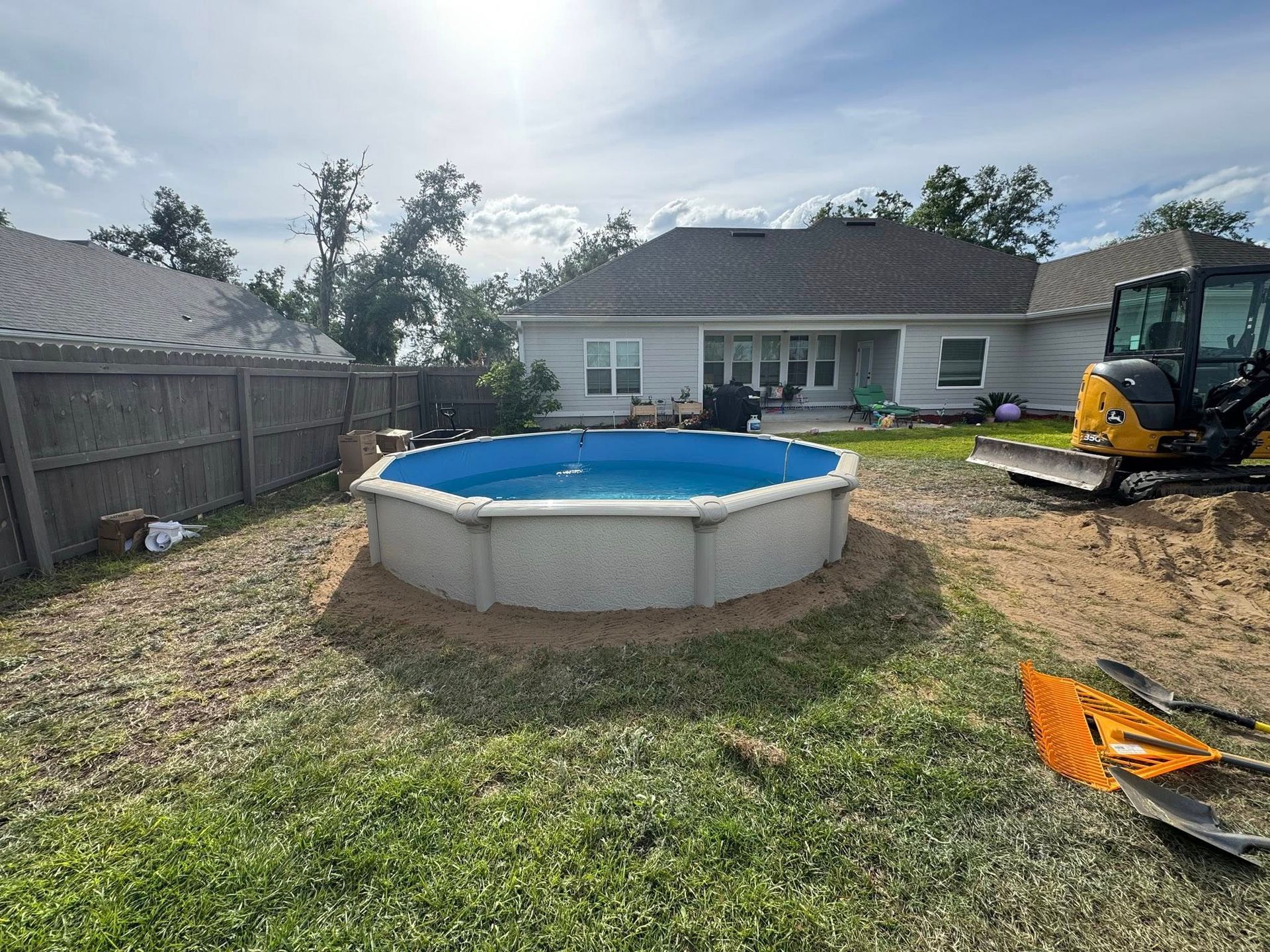 Above-ground pool in a backyard, surrounded by dirt. A small excavator is nearby.