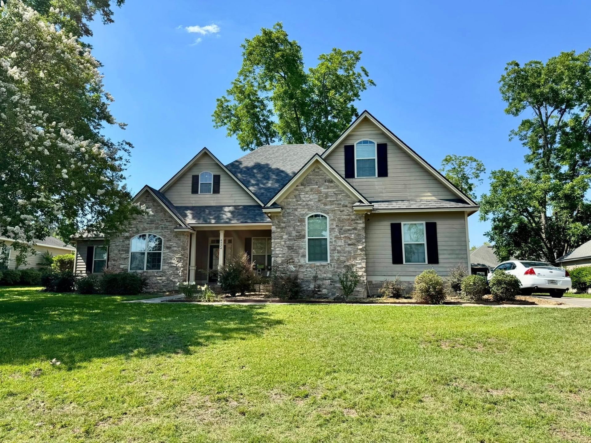 Tan house with stone facade, dark shutters, green lawn, and a blue sky.