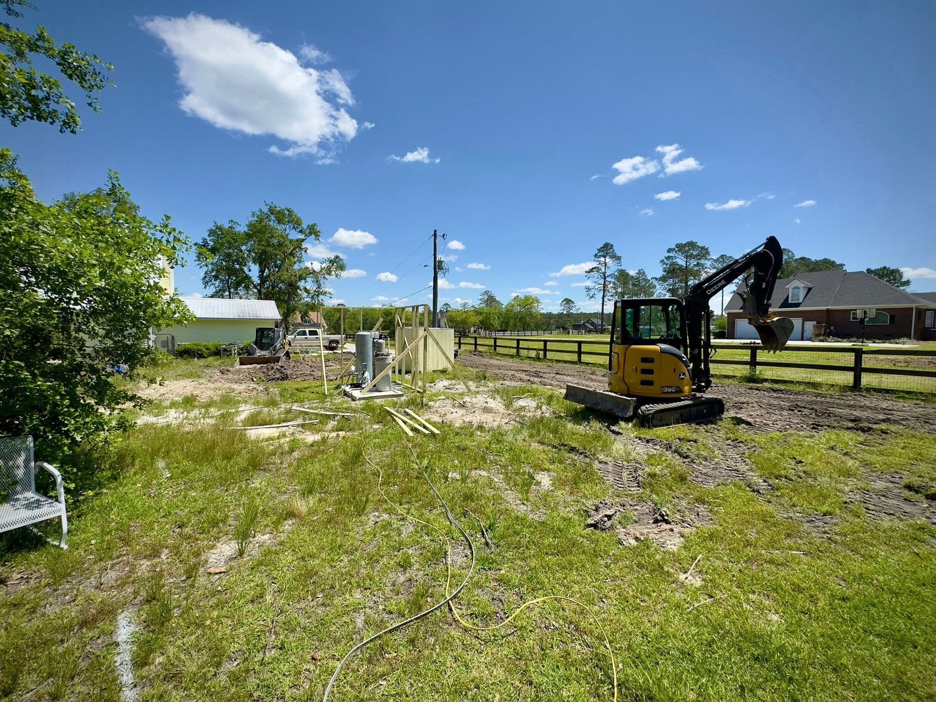 Construction site with a small excavator, sunny day, blue sky, and a partially cleared lot.