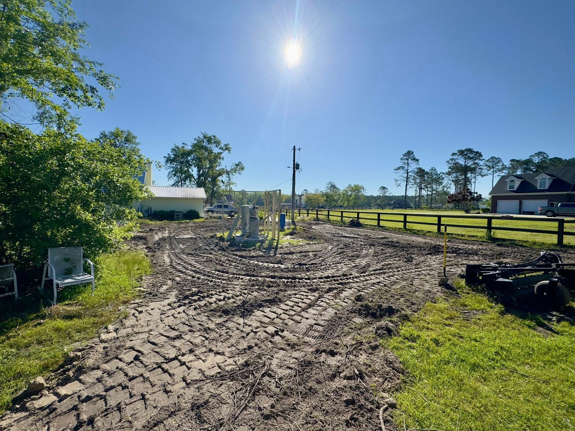 Muddy construction site with tire tracks, blue sky, and a bright sun.