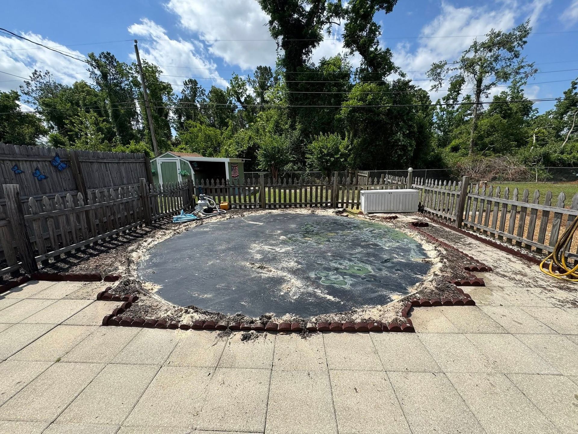 Backyard with a pool covered by a dark cover, surrounded by a fence and patio.