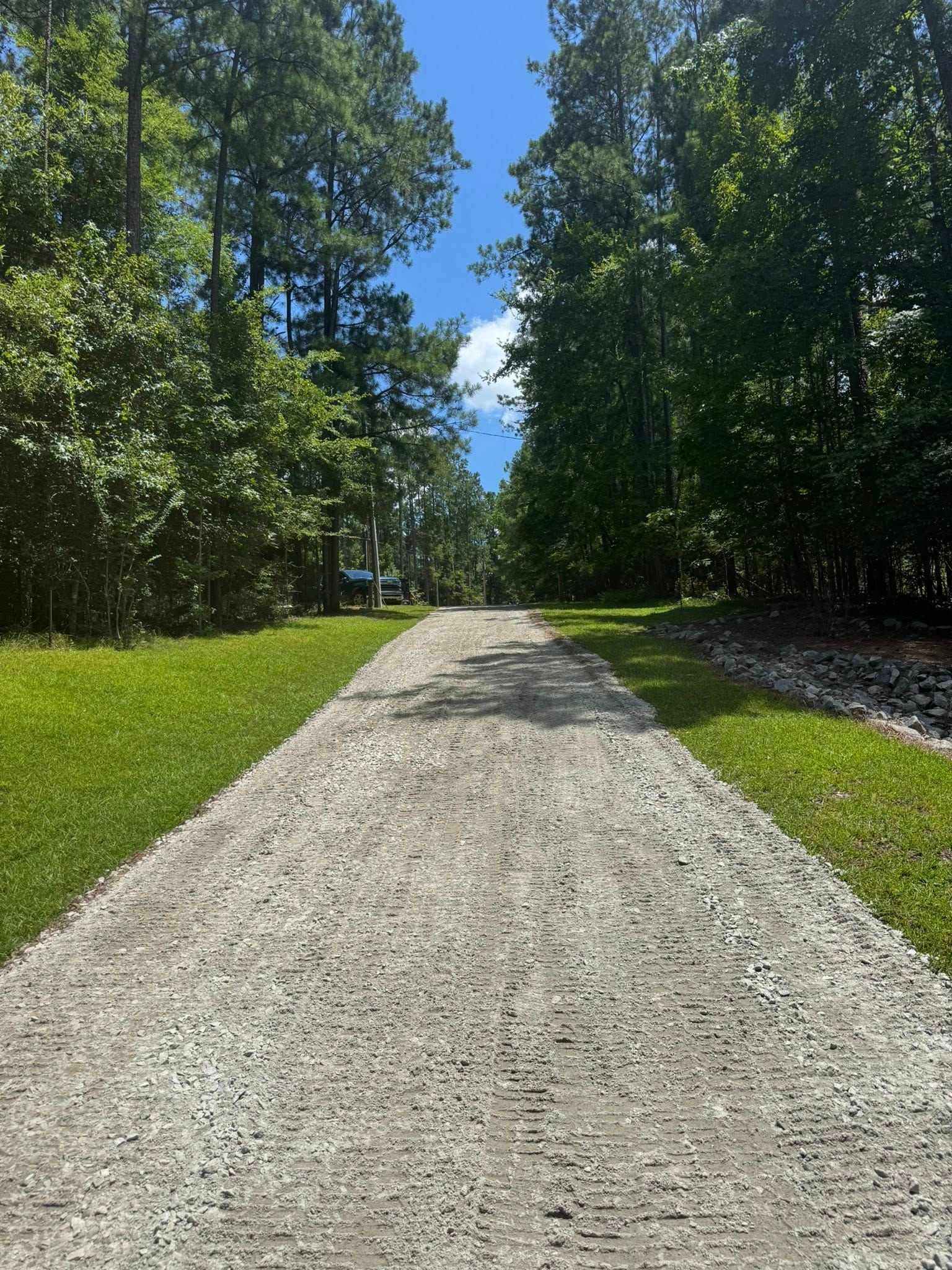 Gravel path lined with green grass and trees, leading toward a clear, blue sky.