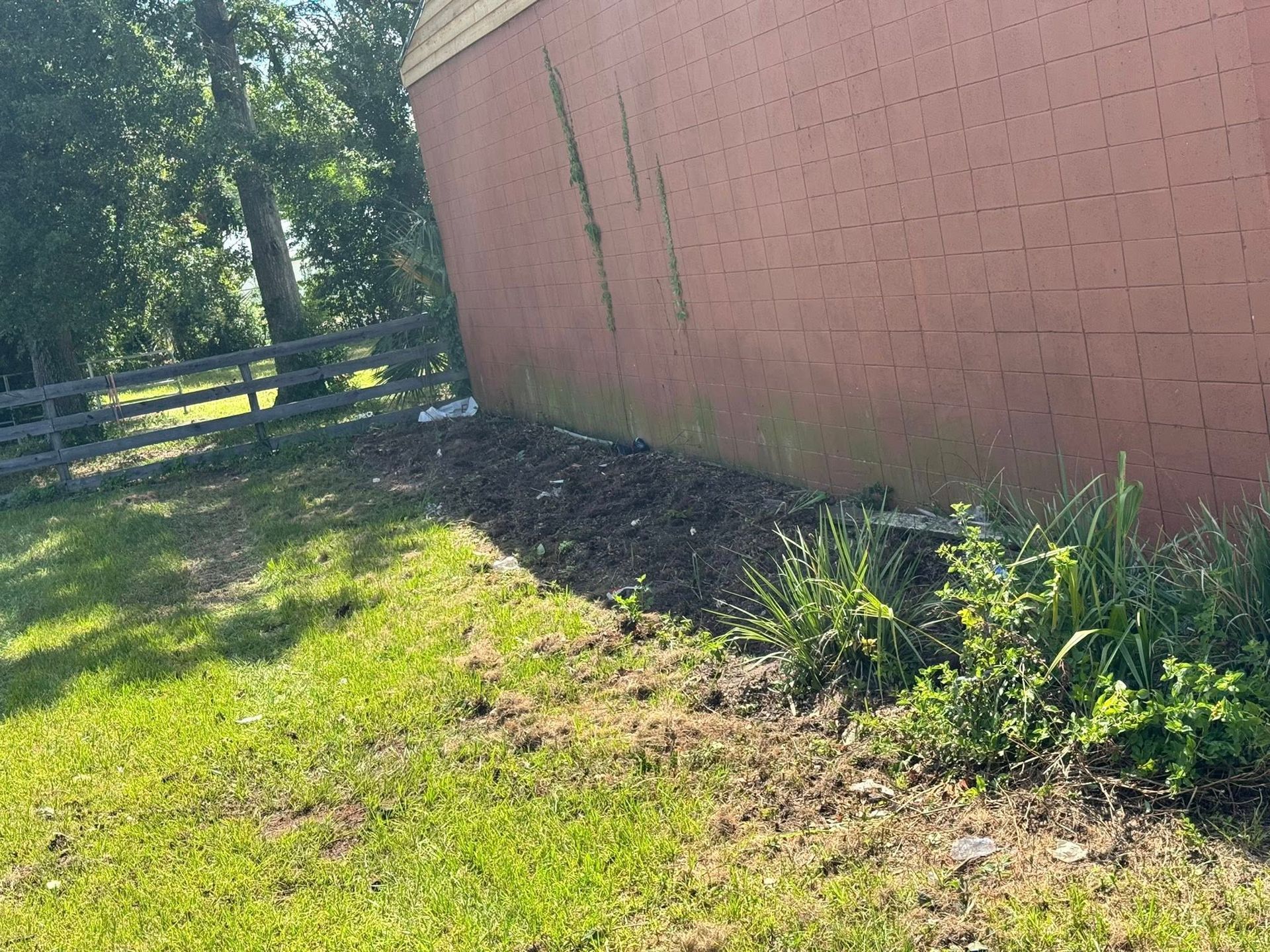 Red brick building with greenery and a wooden fence on a sunny day.