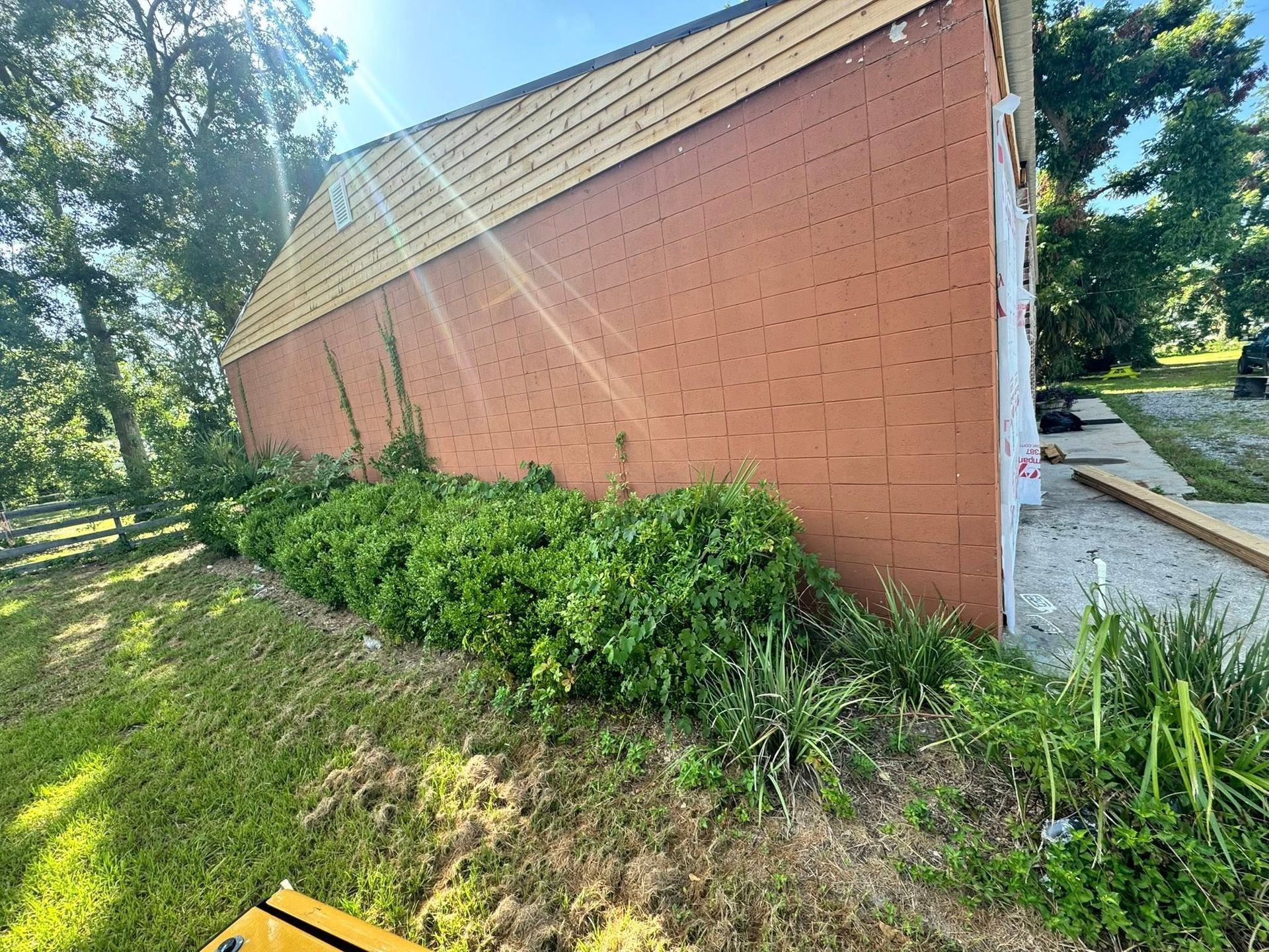 Red brick building with a tan roof, overgrown with green plants, on a grassy hill.