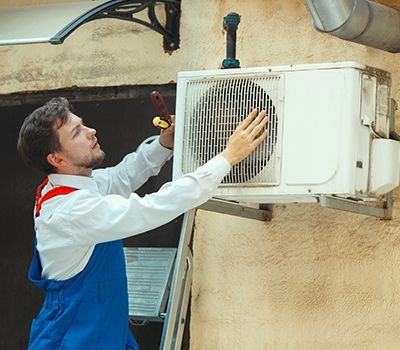 A man is fixing an air conditioner on the side of a building.