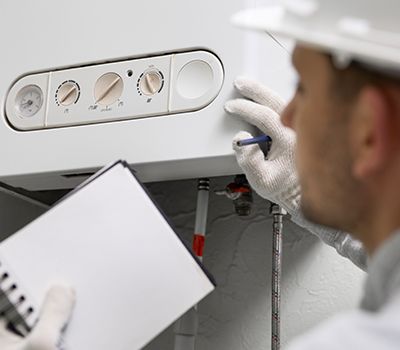 A man is working on a boiler while holding a clipboard.