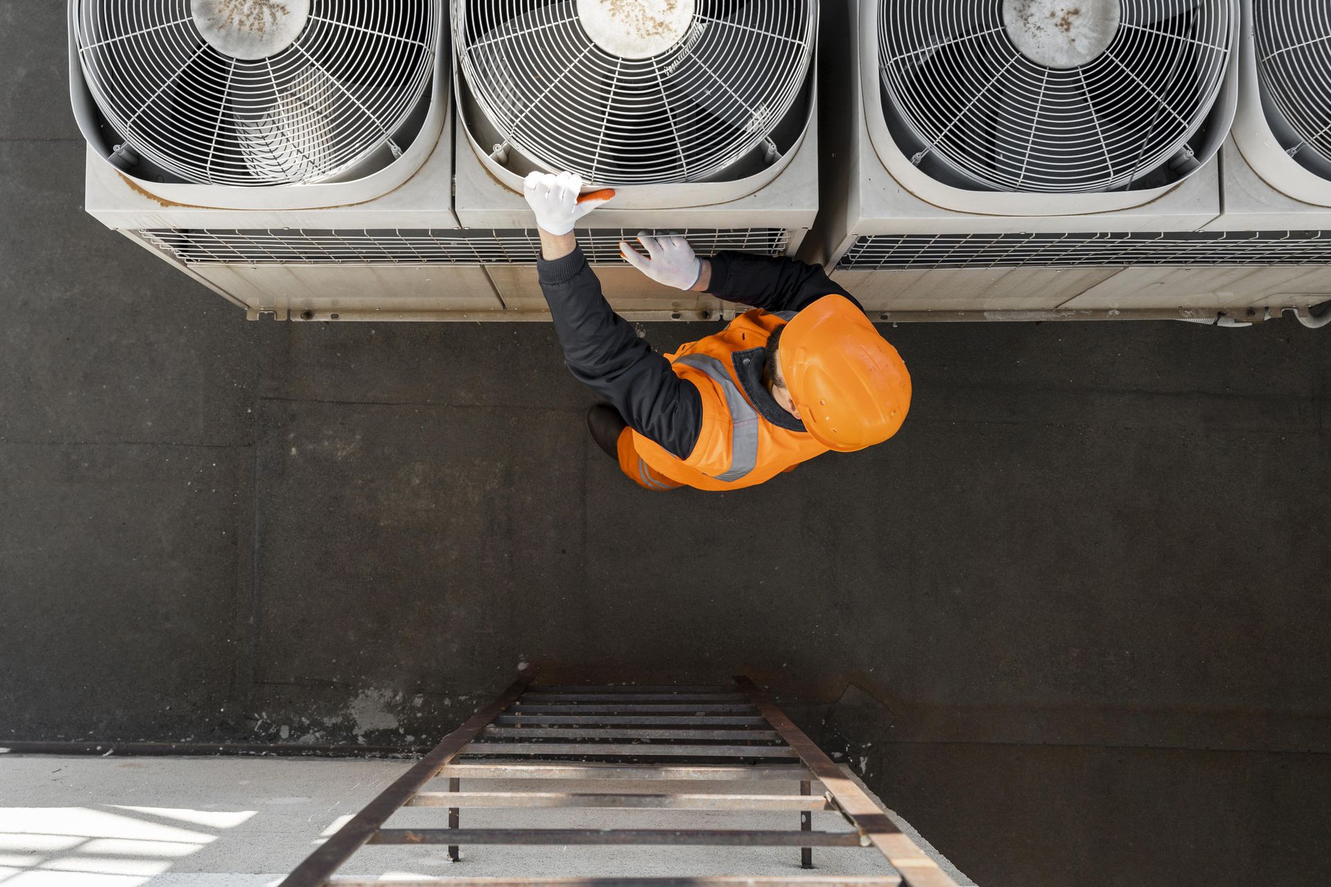 A man is standing on a ladder working on an air conditioner.