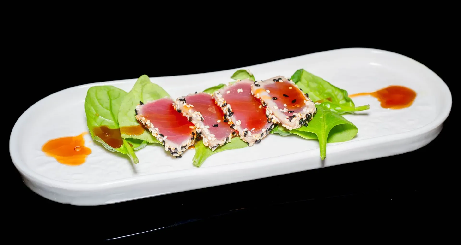 Sushi a fette su un piatto bianco con guarnizione verde e salsa arancione a filo.