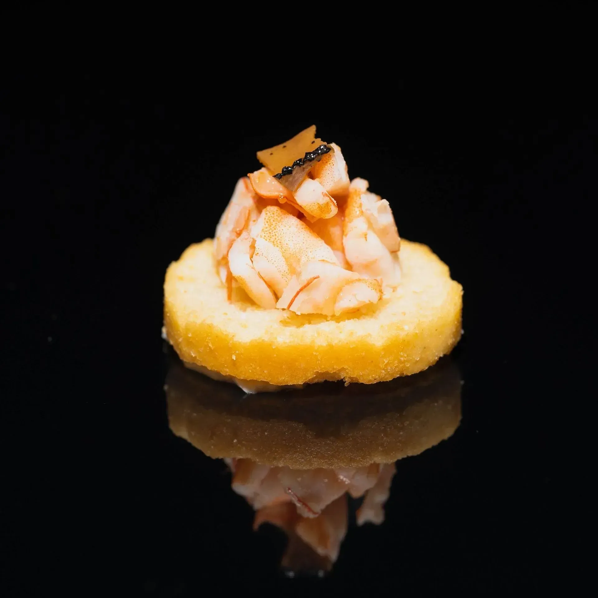 Mini crostata con crema rosa e guarnizione, su sfondo nero riflettente.