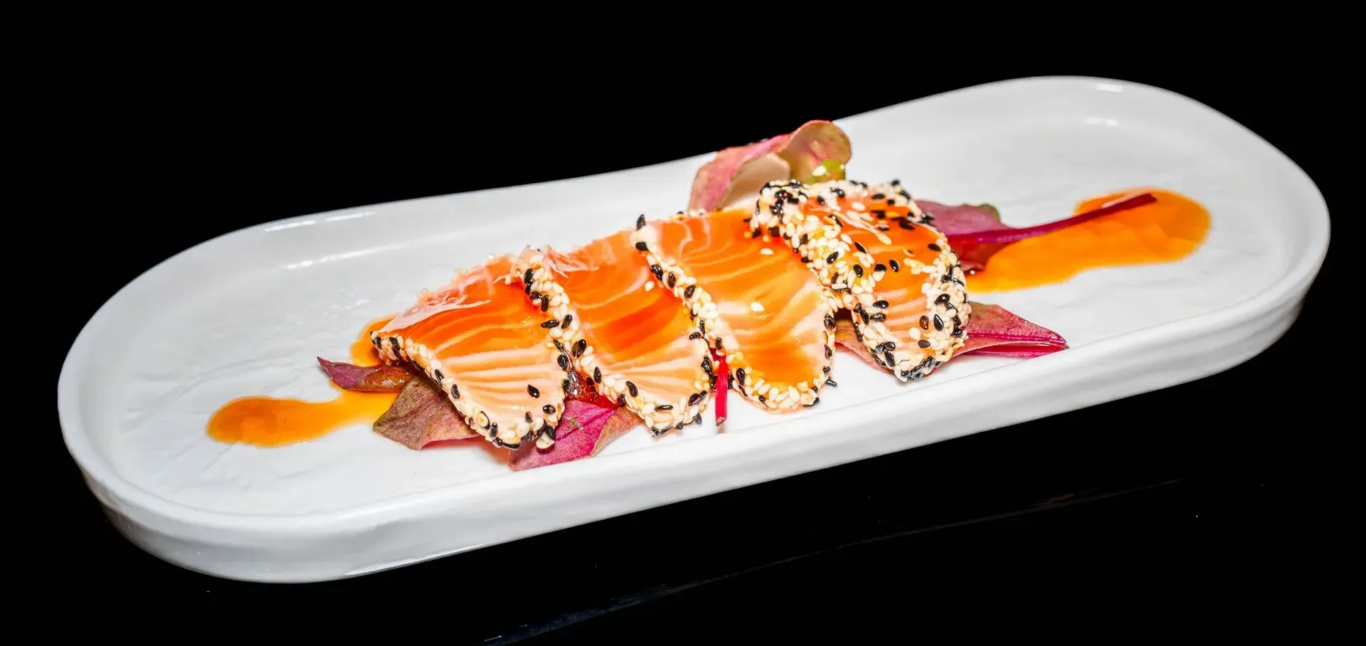 Rotoli di sushi con salsa all'arancia e semi di sesamo su un piatto rettangolare bianco.