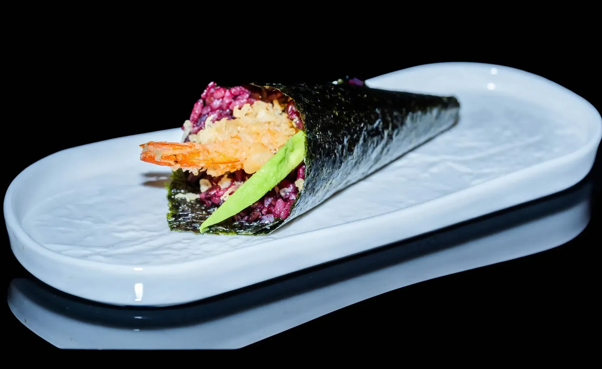 Sushi hand roll con ripieni colorati su un piatto da portata bianco.