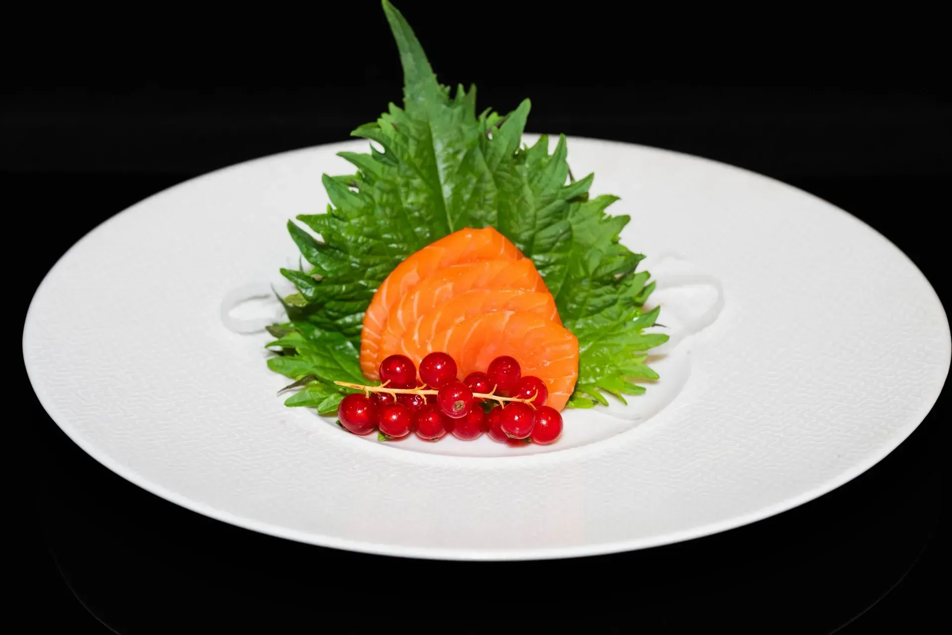 Filetto di salmone su un letto di verdure con frutti rossi, disposto su un piatto bianco.