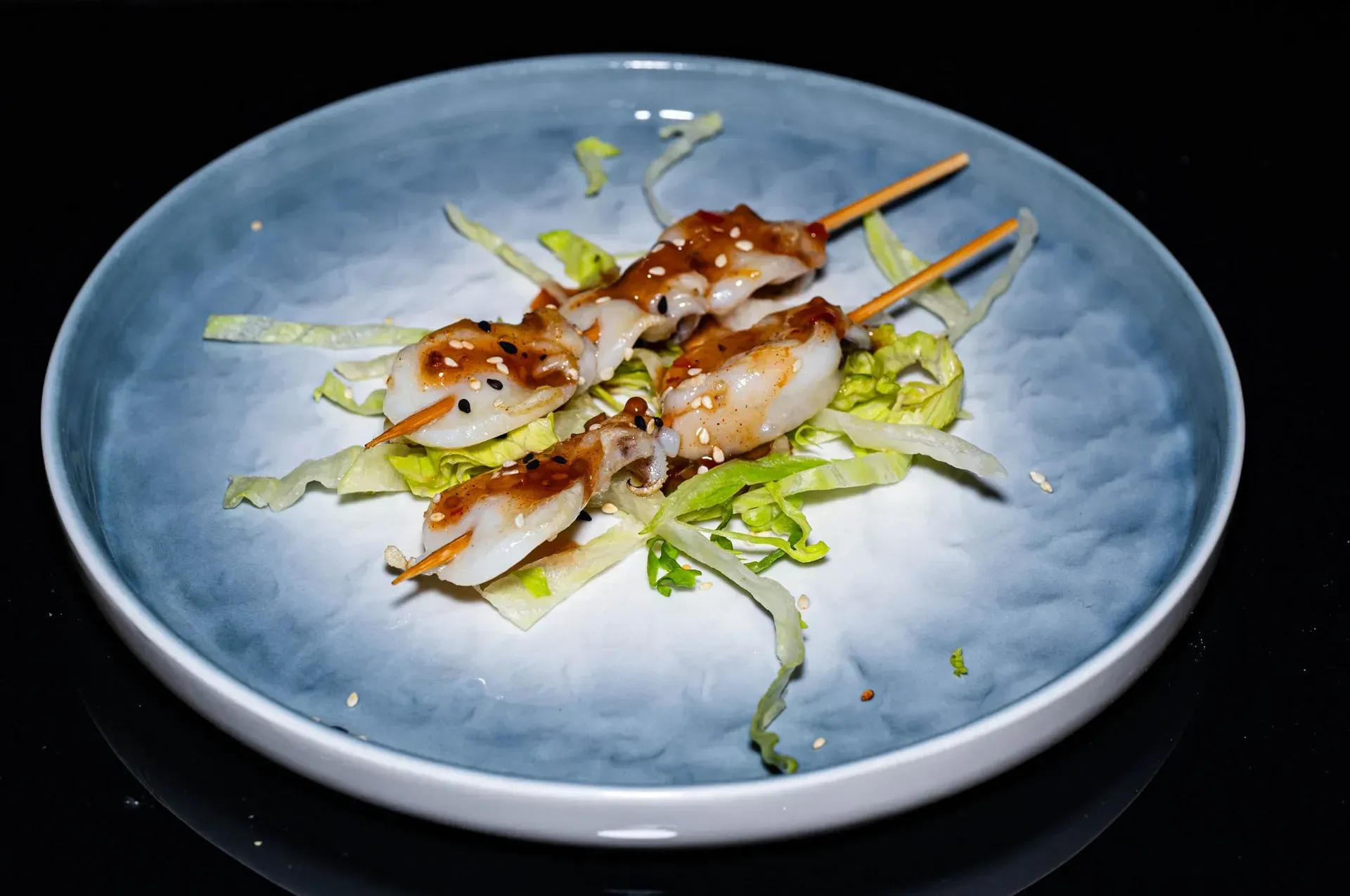 Spiedini di gamberi grigliati su un letto di verdure tritate, serviti su un piatto blu.