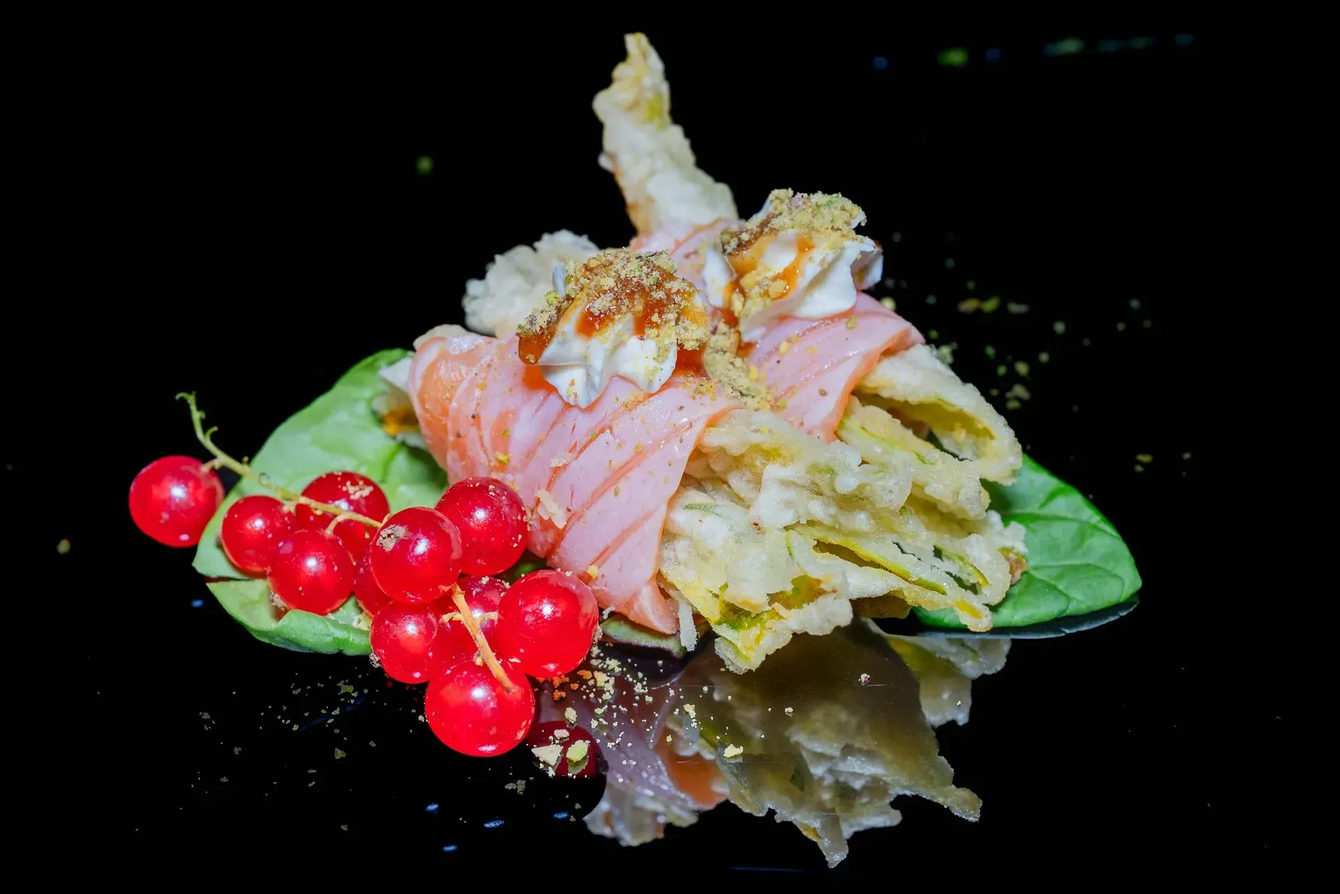 Dessert con crema rosa, frutti di bosco e foglie di menta su sfondo nero.