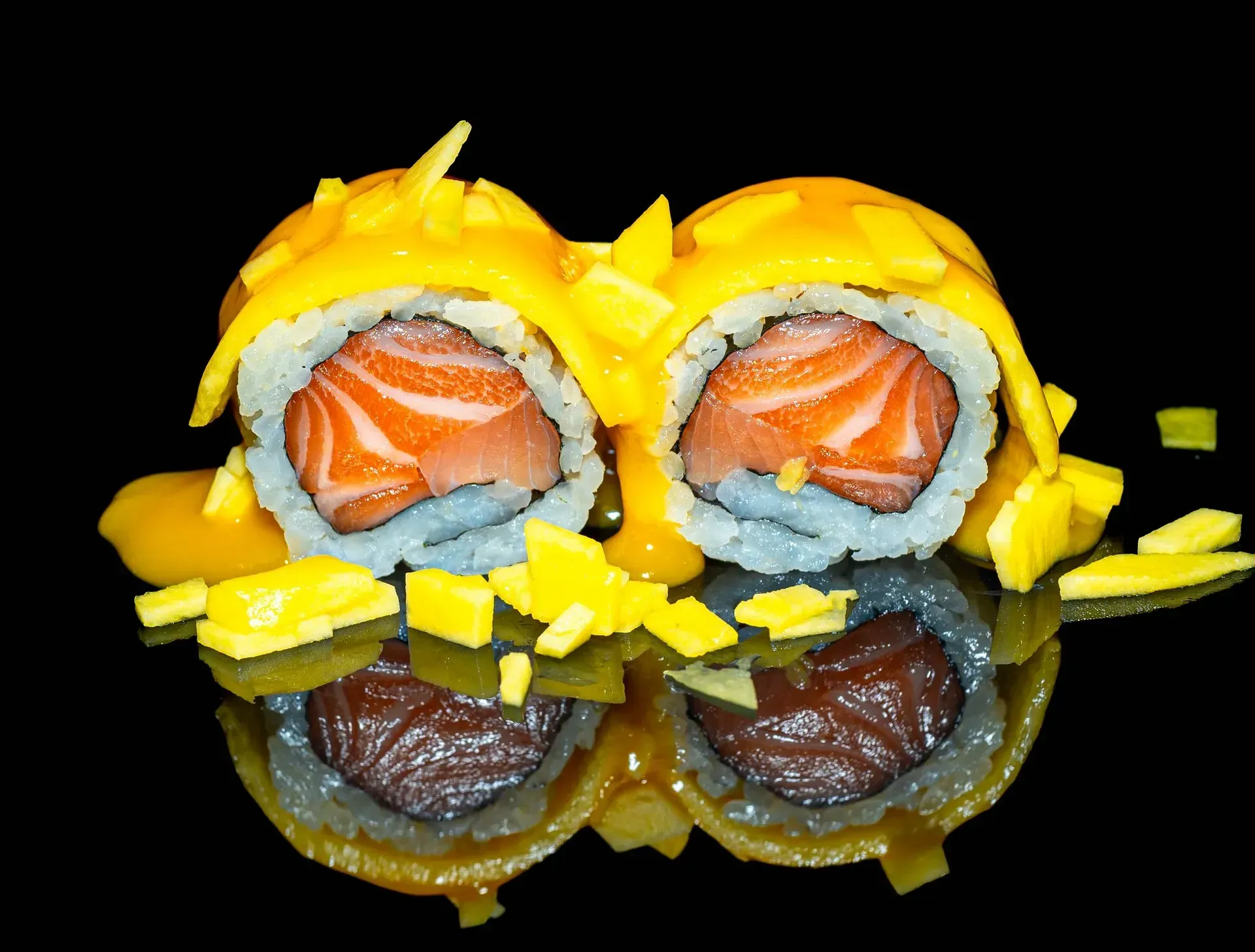 Assortimento di involtini di sushi con salmone e alghe scure, guarniti con una decorazione gialla su sfondo nero.