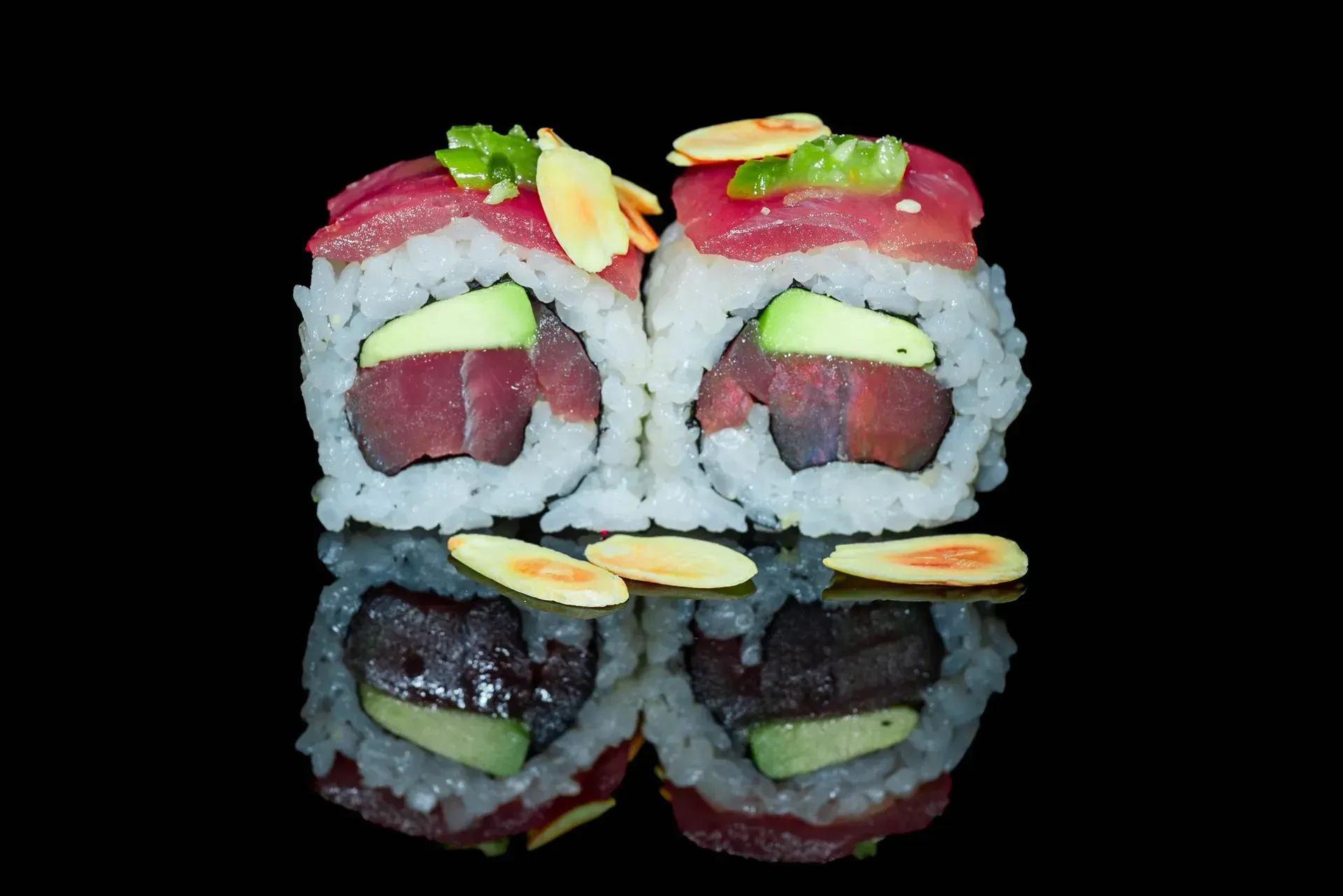 Rotoli di sushi con pesce rosso e guarnizione verde, riflessi su una superficie nera lucida.
