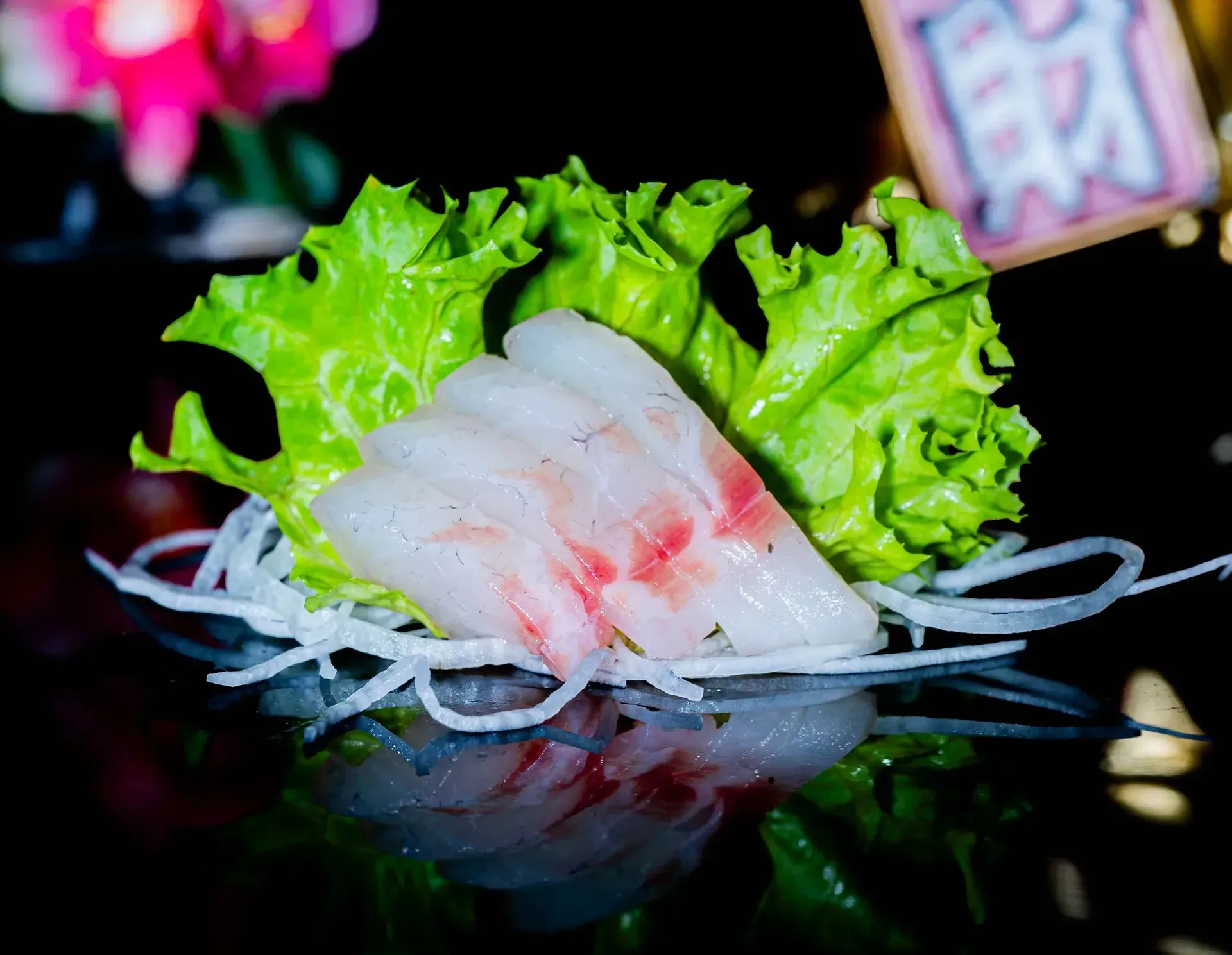 Fette di sashimi di pesce bianco su un letto di lattuga e daikon grattugiato, servite su un piatto nero lucido.