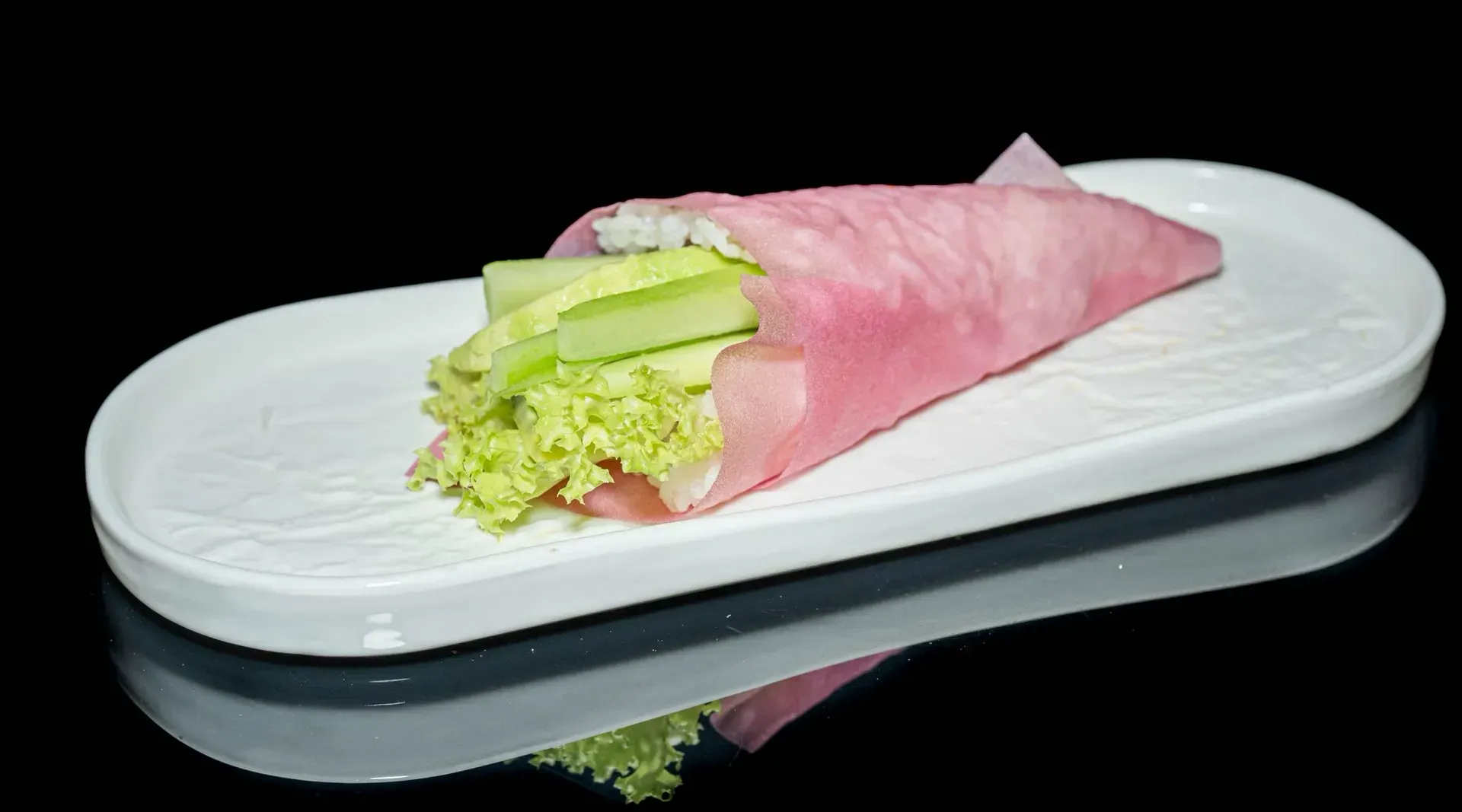 Panino avvolto in carta rosa su un piatto ovale bianco su sfondo nero.