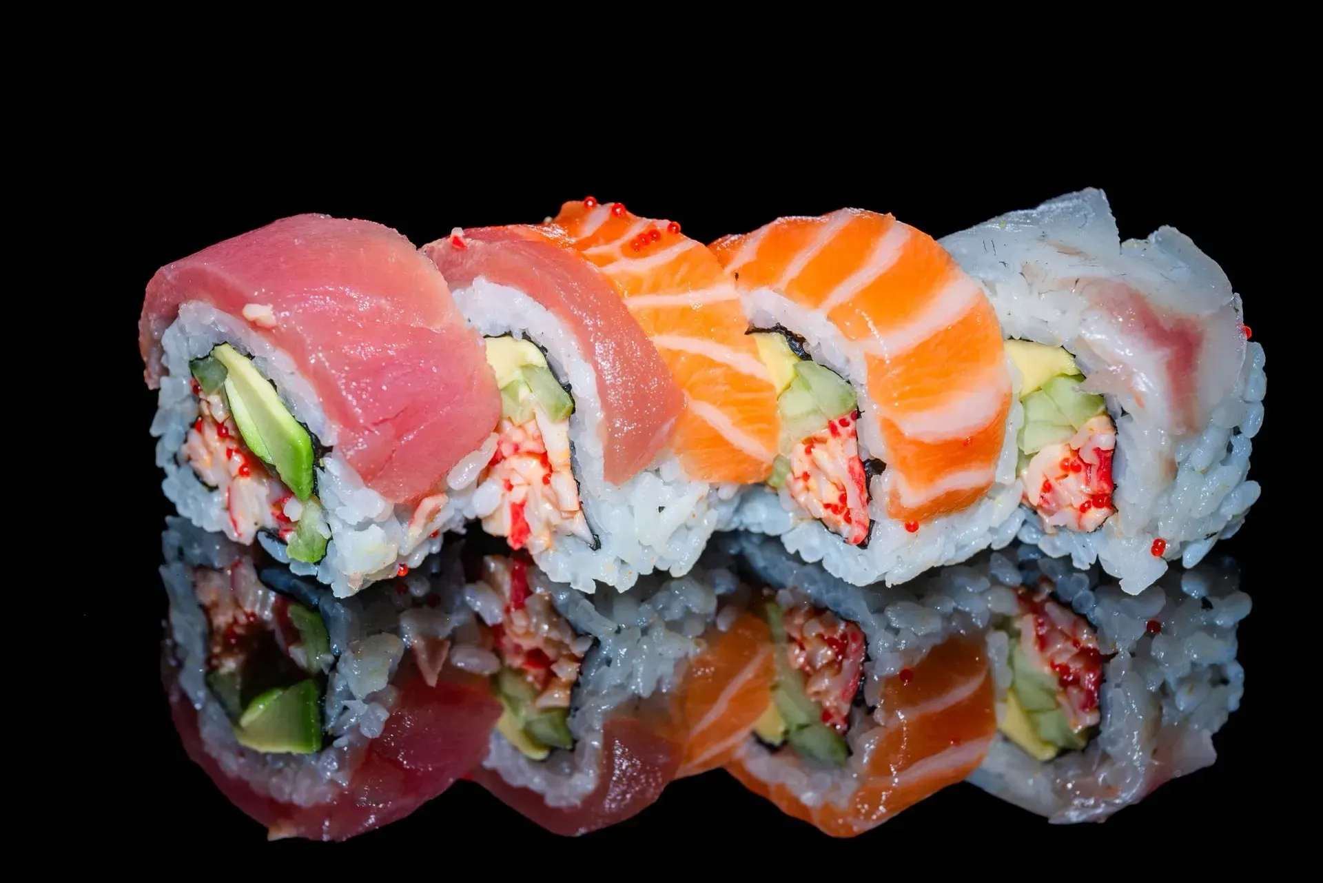 Pezzi di sushi colorati con salmone e tonno, riflessi su una superficie nera.