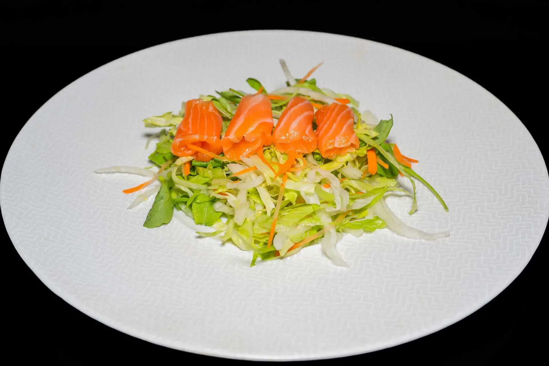 Sashimi di salmone su un letto di lattuga tritata in un piatto bianco.