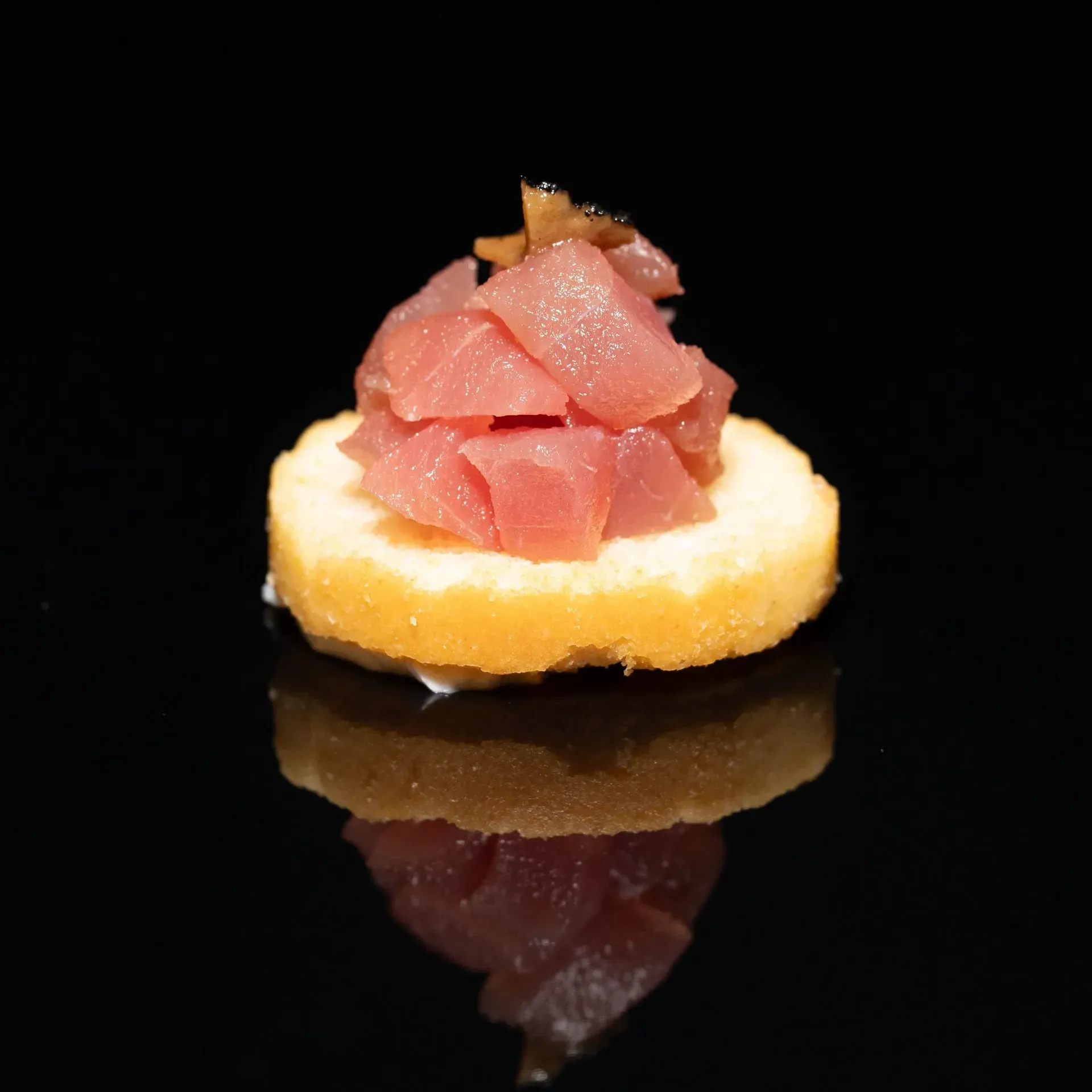 Sushi nigiri guarnito con tonno a cubetti su una superficie nera riflettente