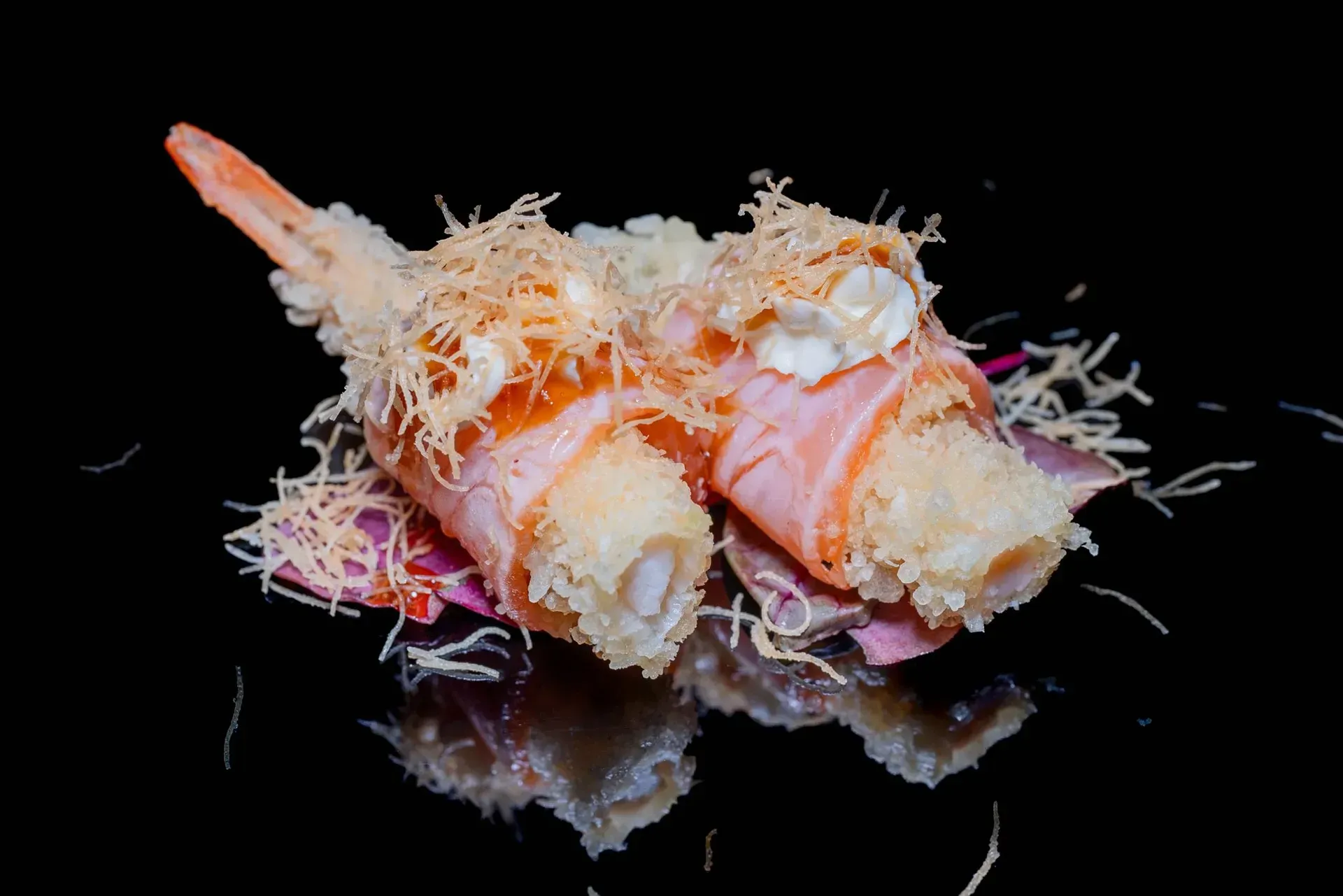 Gamberi cotti guarniti con una decorazione sminuzzata su una superficie nera riflettente