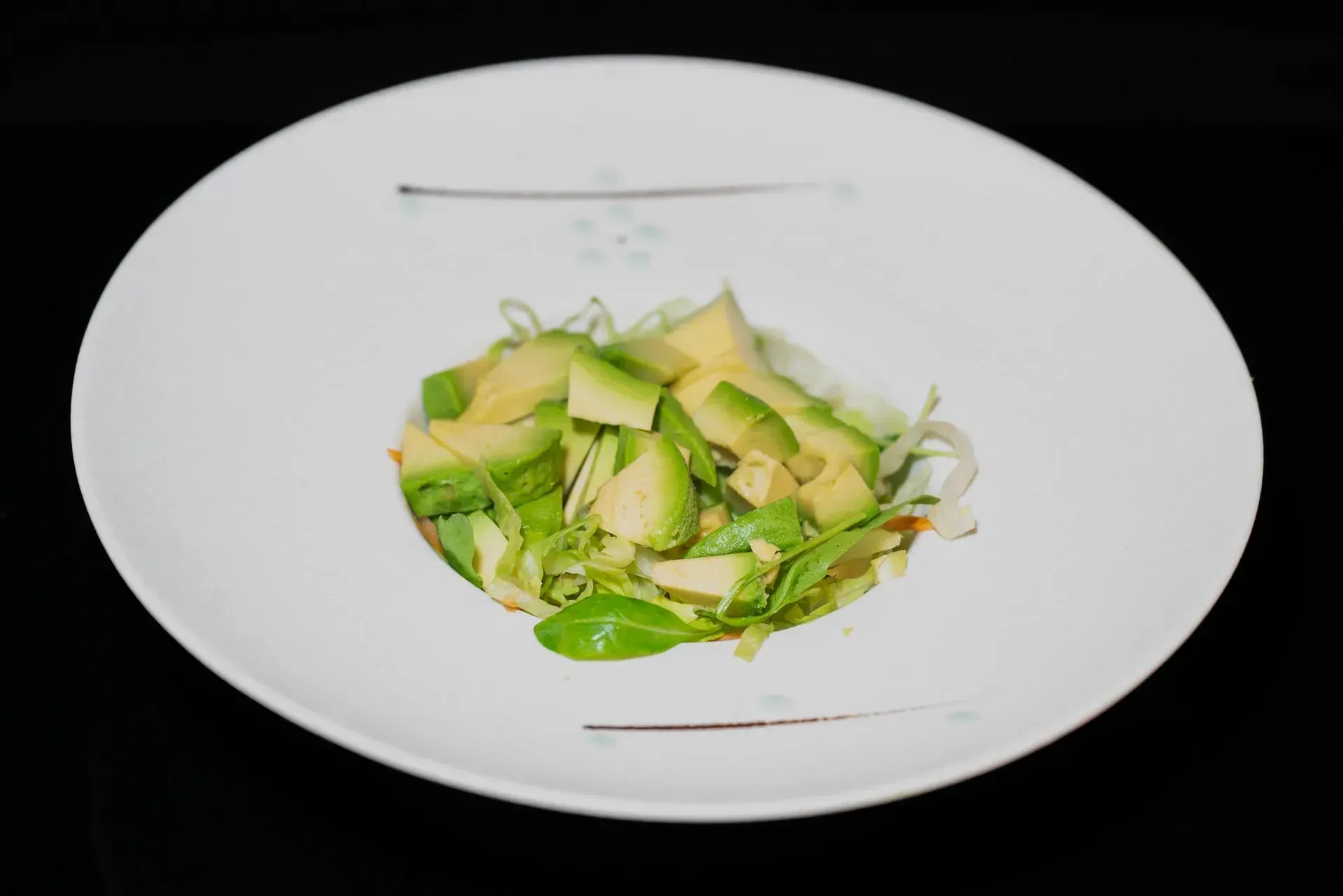 Insalata verde con avocado a fette su un piatto bianco.