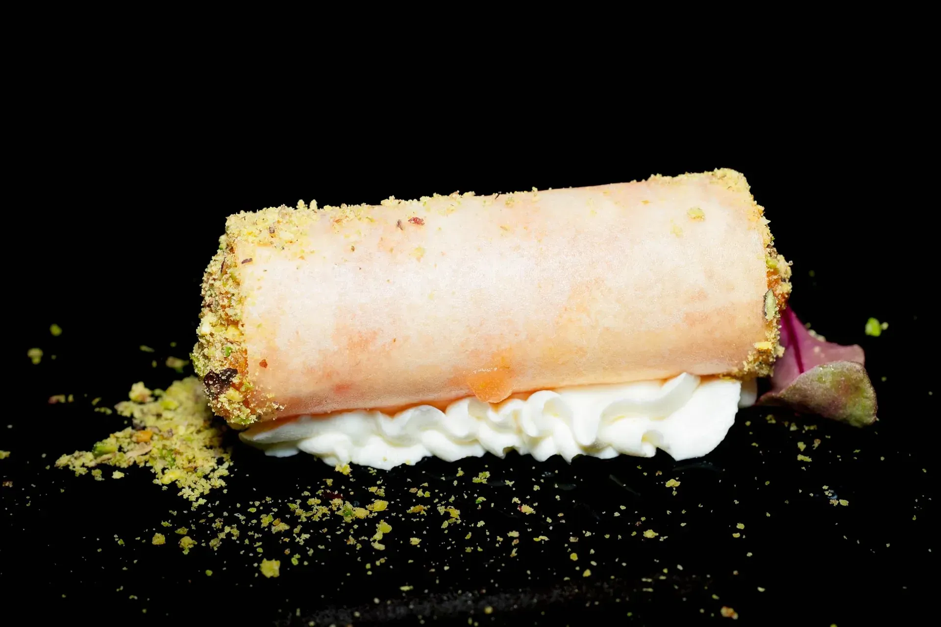 Torta arrotolata di pasta frolla con ripieno di crema e copertura di briciole su sfondo nero.