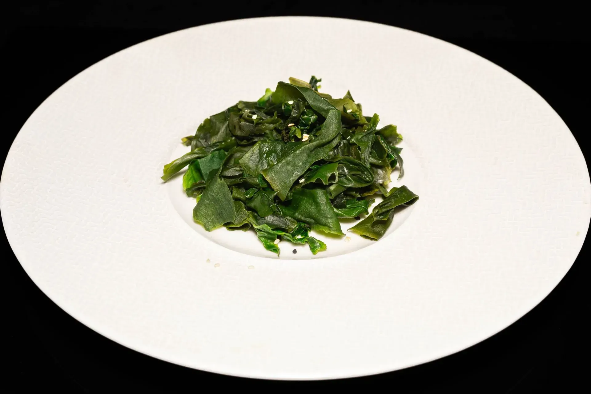 Una piccola porzione di verdure a foglia verde lucido su un piatto bianco.