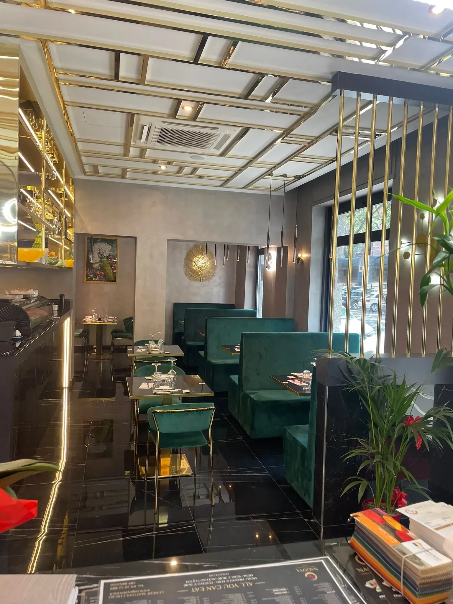 Interni moderni di un ristorante con divanetti in velluto verde, tavoli neri e decorazioni elaborate sul soffitto.