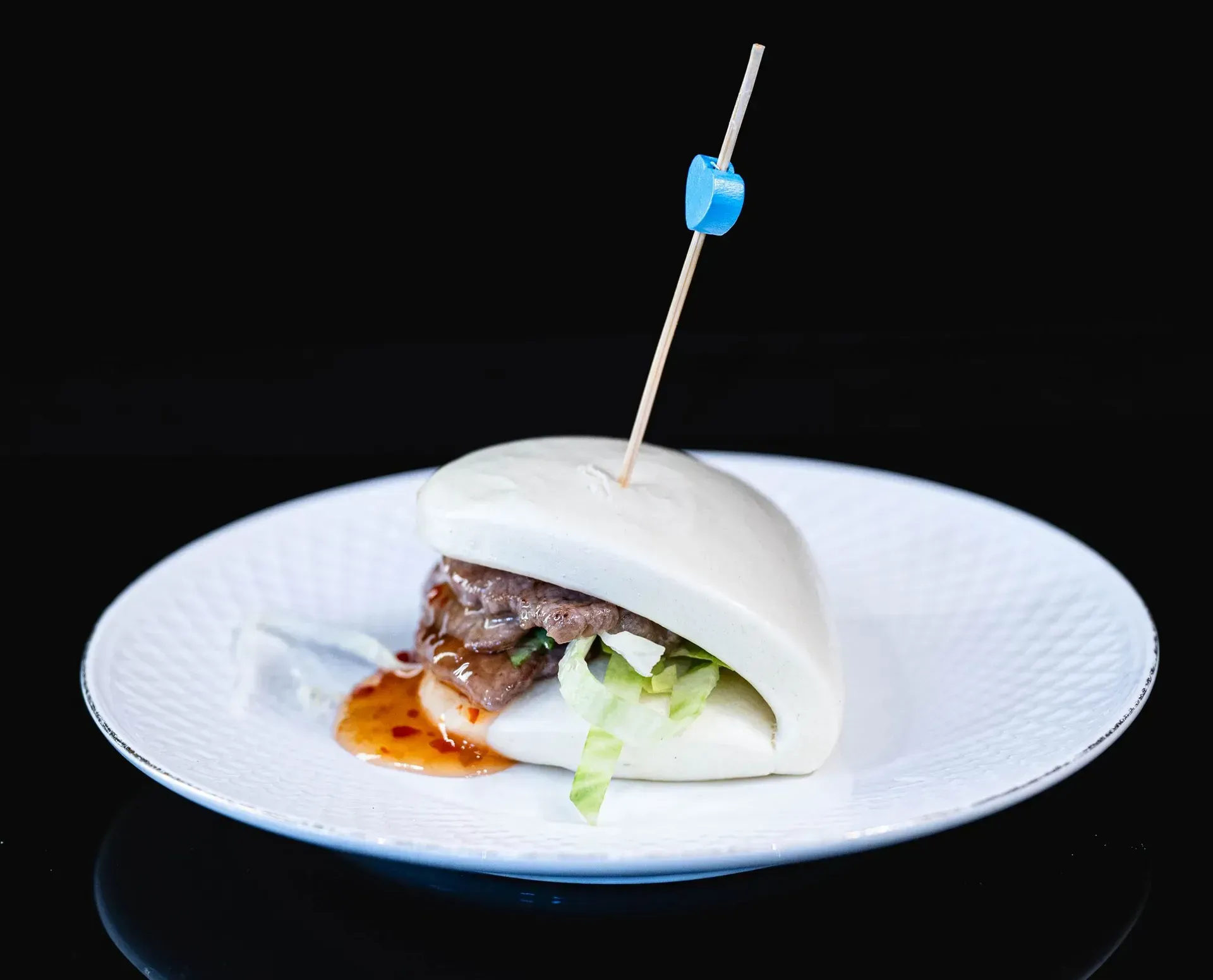 Panino con pane bianco, lattuga e salsa su un piatto, sormontato da uno spiedino, su sfondo nero.