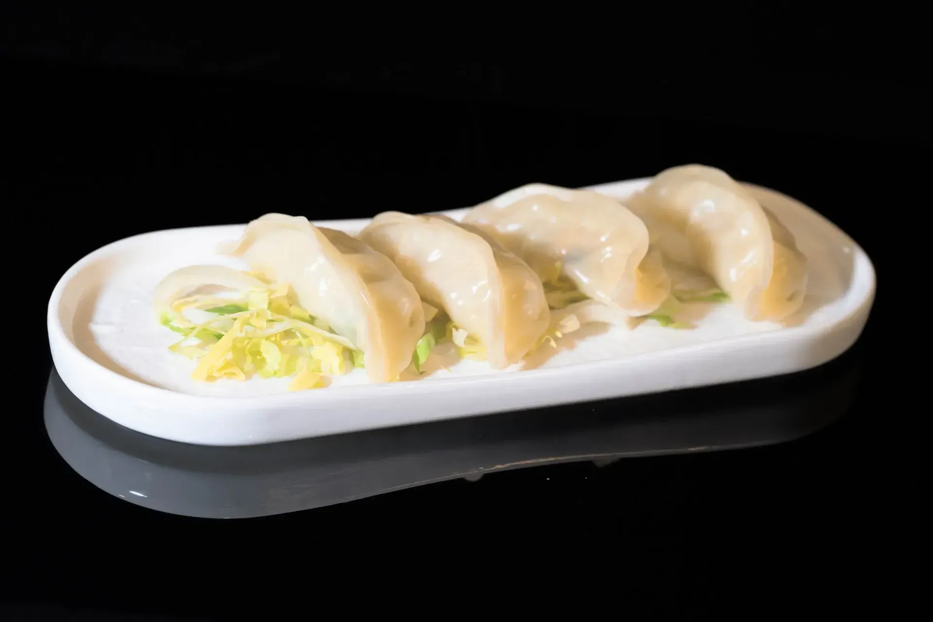 Ravioli su un piatto ovale bianco con una piccola guarnizione su sfondo nero.