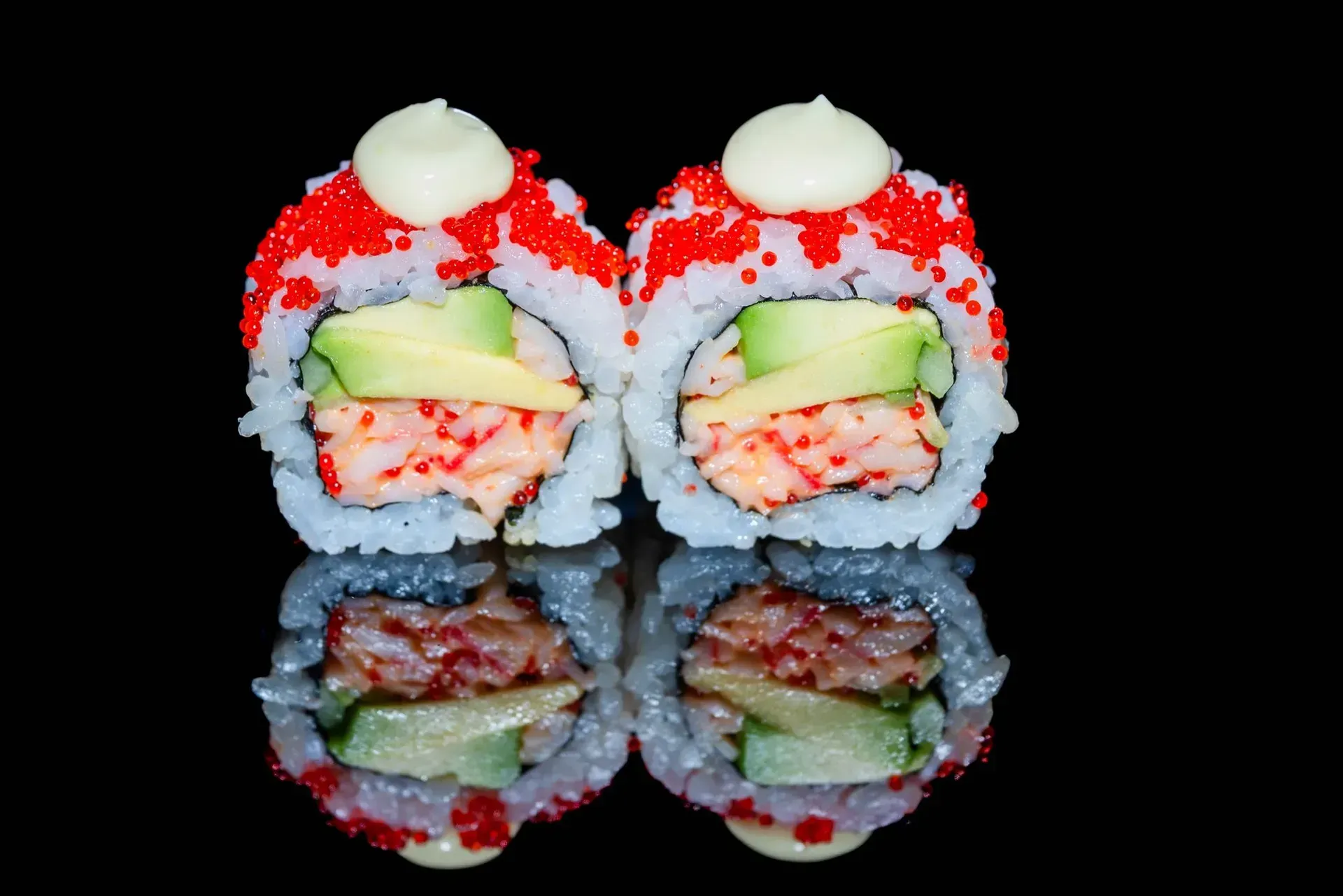 Due coloratissimi rotolini di sushi con guarnizione bianca, specchiati su una superficie nera lucida