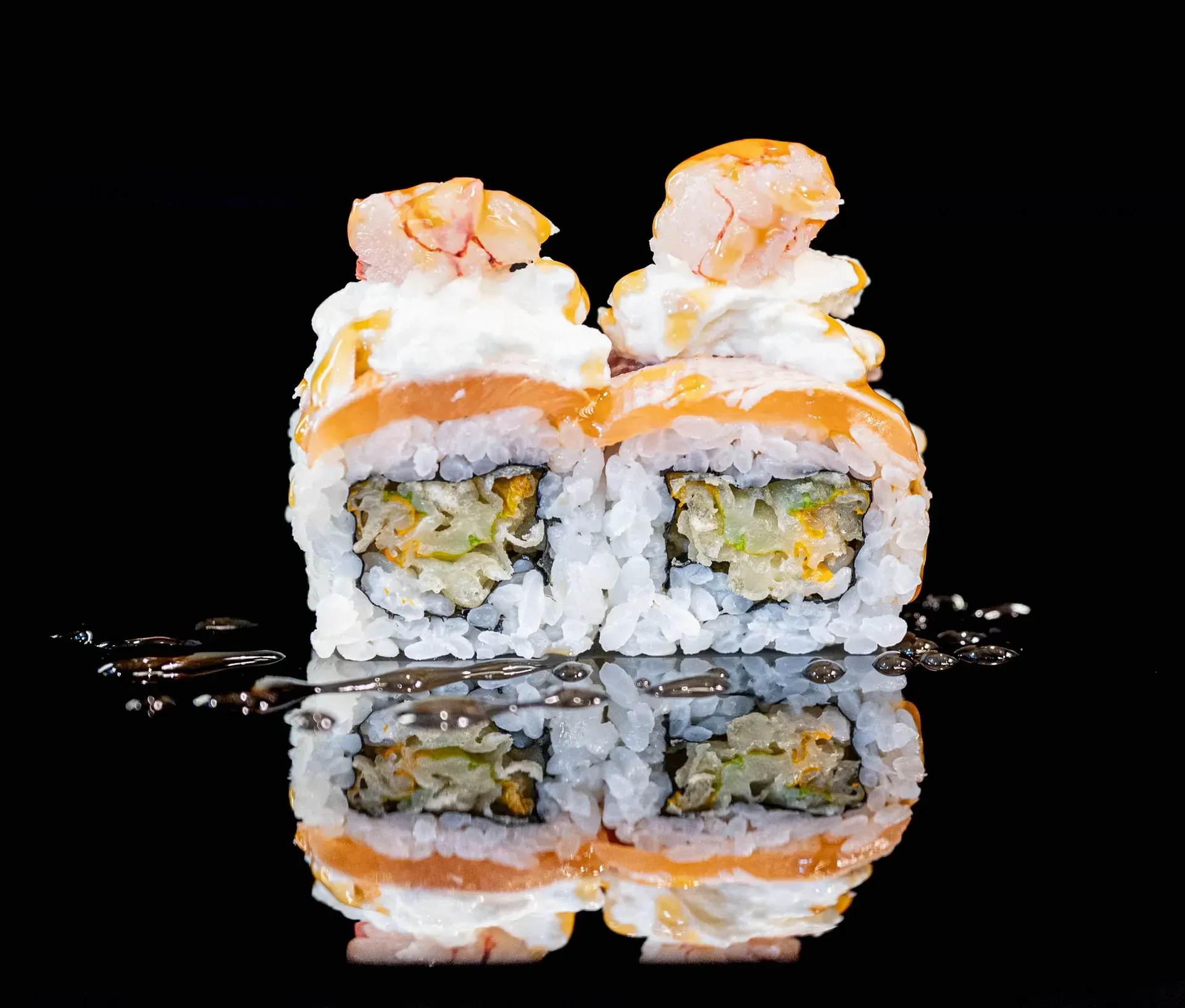 Rotoli di sushi guarniti con salmone e panna, riflessi su una superficie nera lucida.