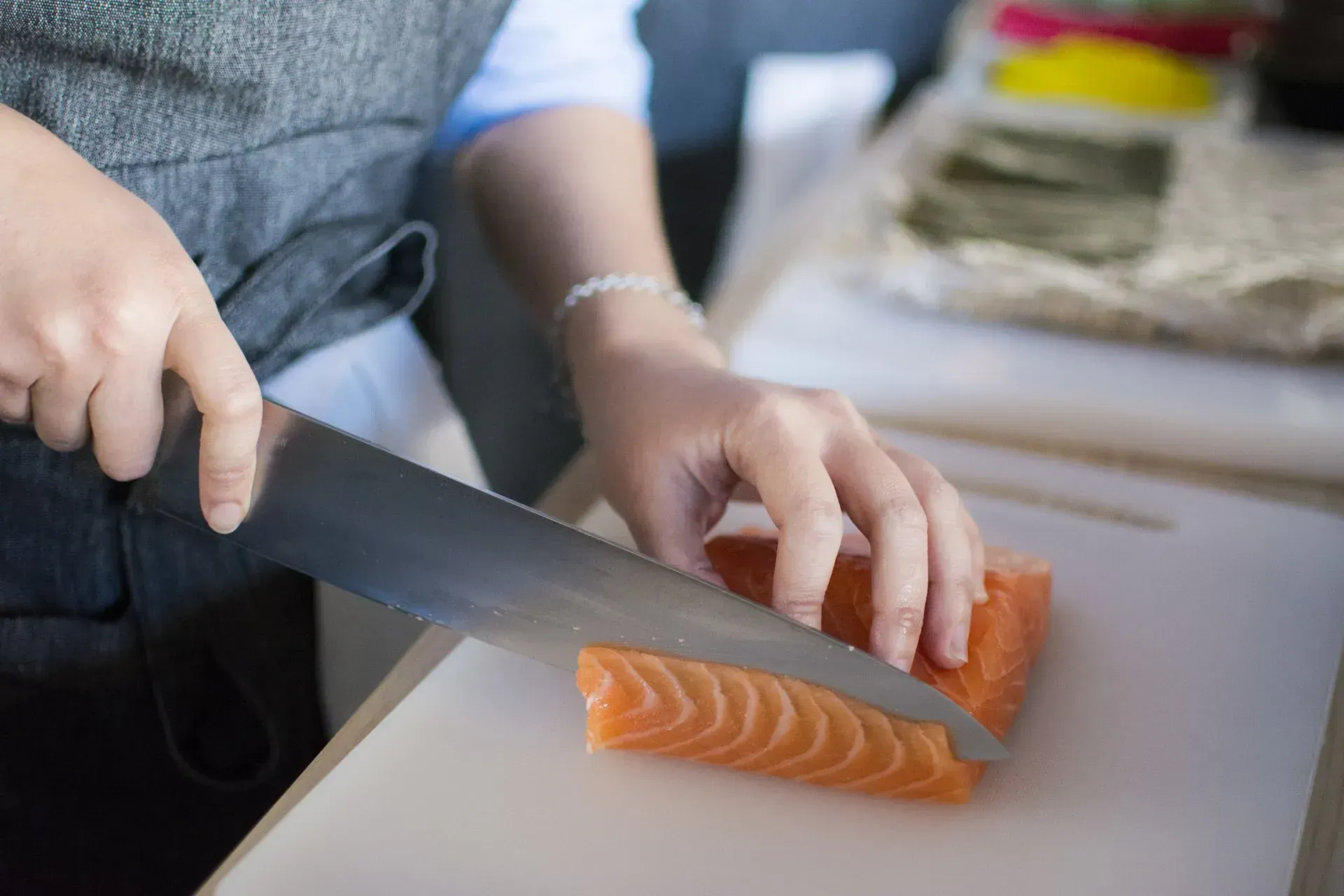 Mani che affettano il salmone su un tagliere con un coltello da chef.