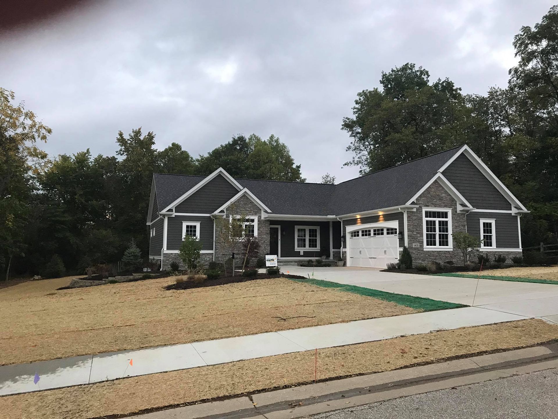 Ranch-style house with dark gray siding, stone accents, and a two-car garage under an overcast sky.