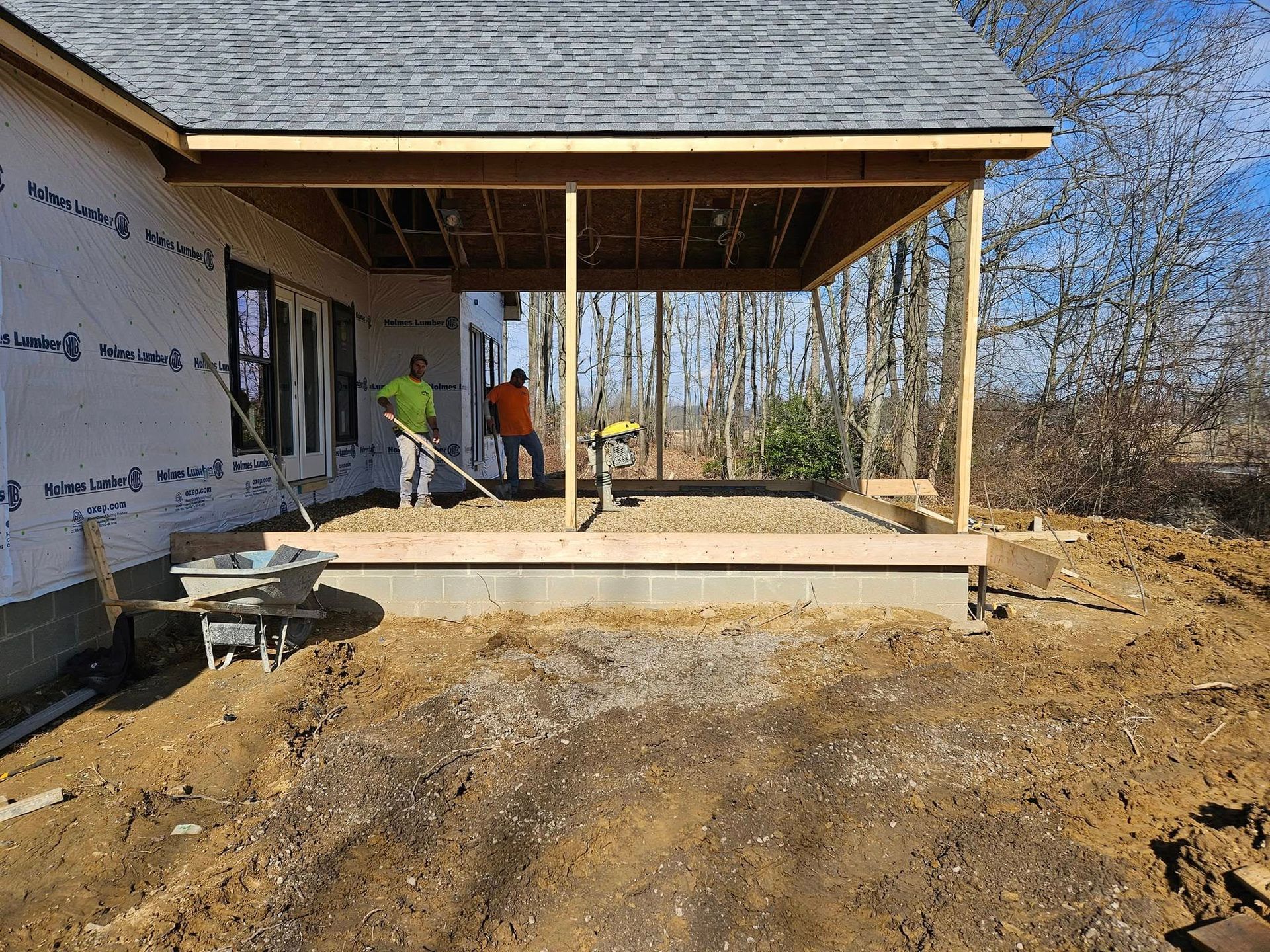 Construction of a covered porch on a house; two workers, wooden supports, and exposed framing.