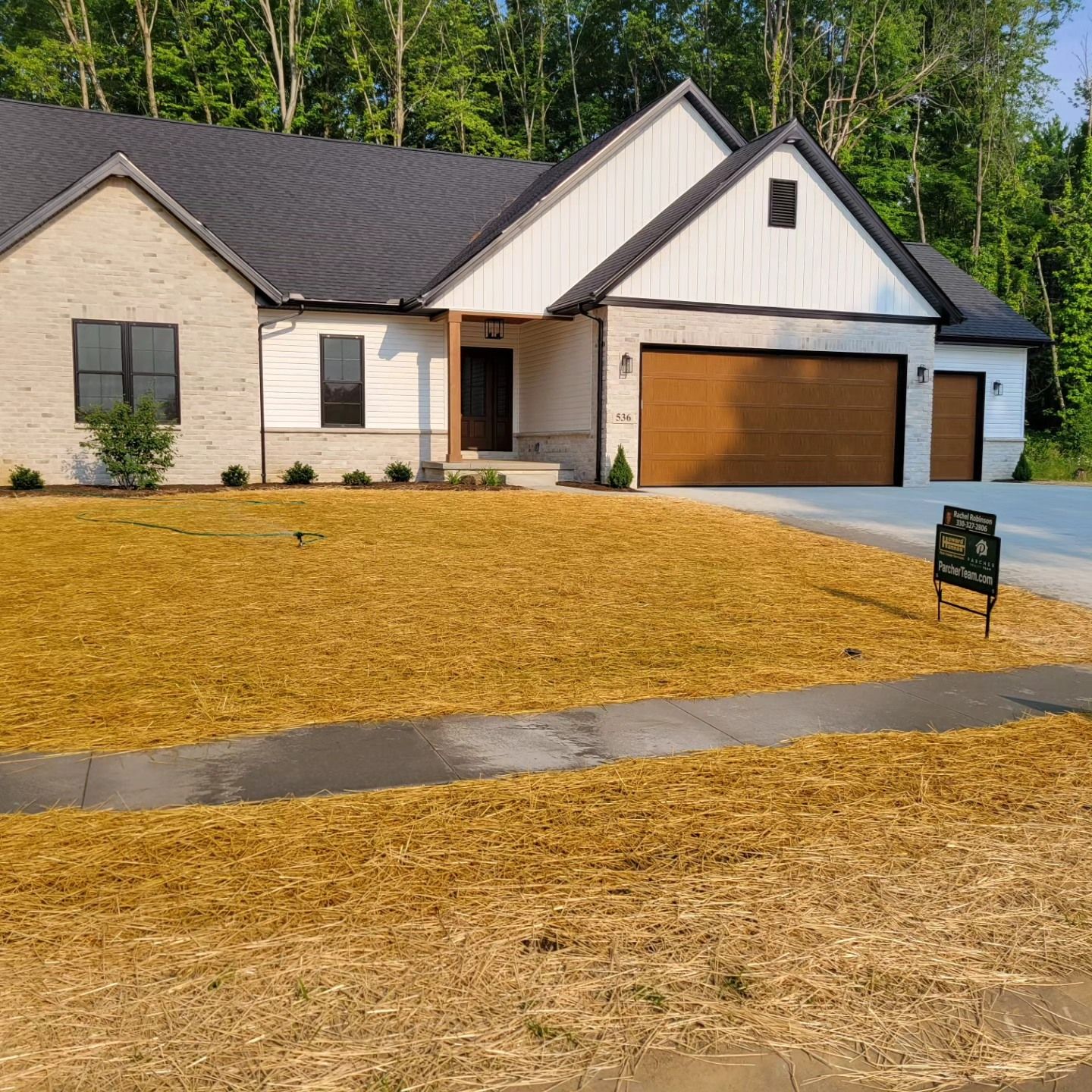 A light-colored brick house with a dark roof and a wood-toned garage door, front lawn with mulch.